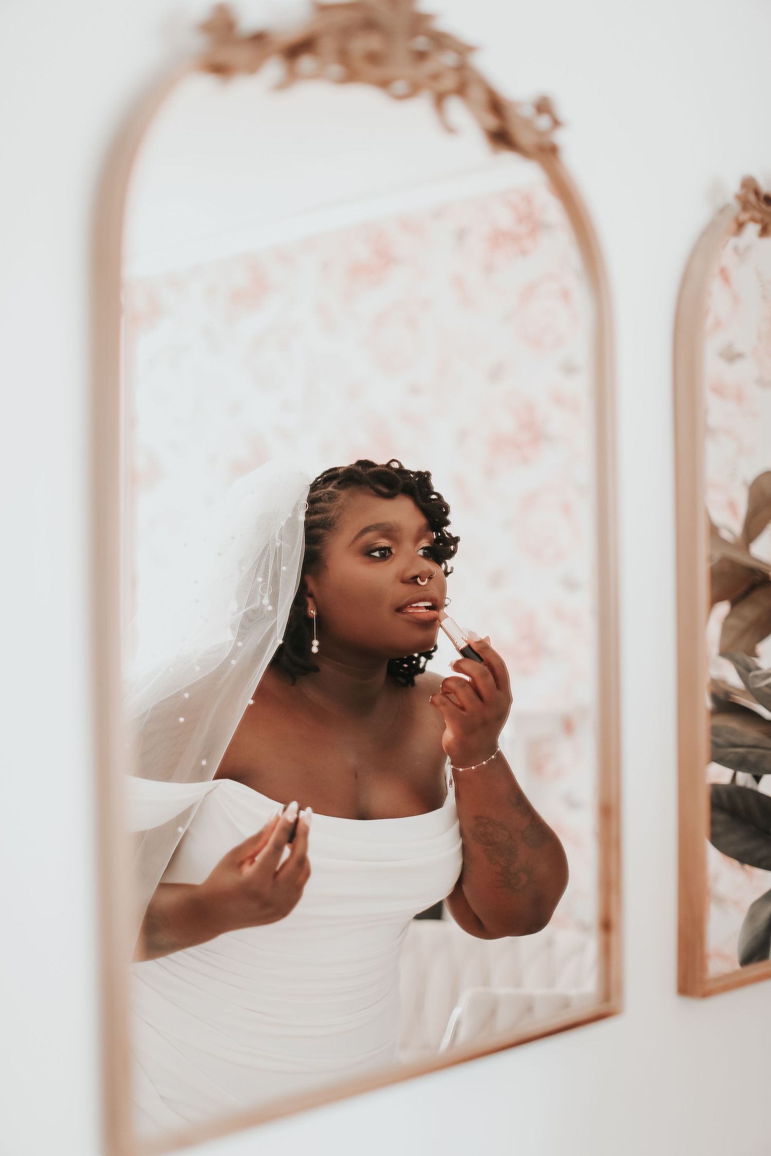 Bride checking her reflection in an elegant arched mirror while adjusting her veil.