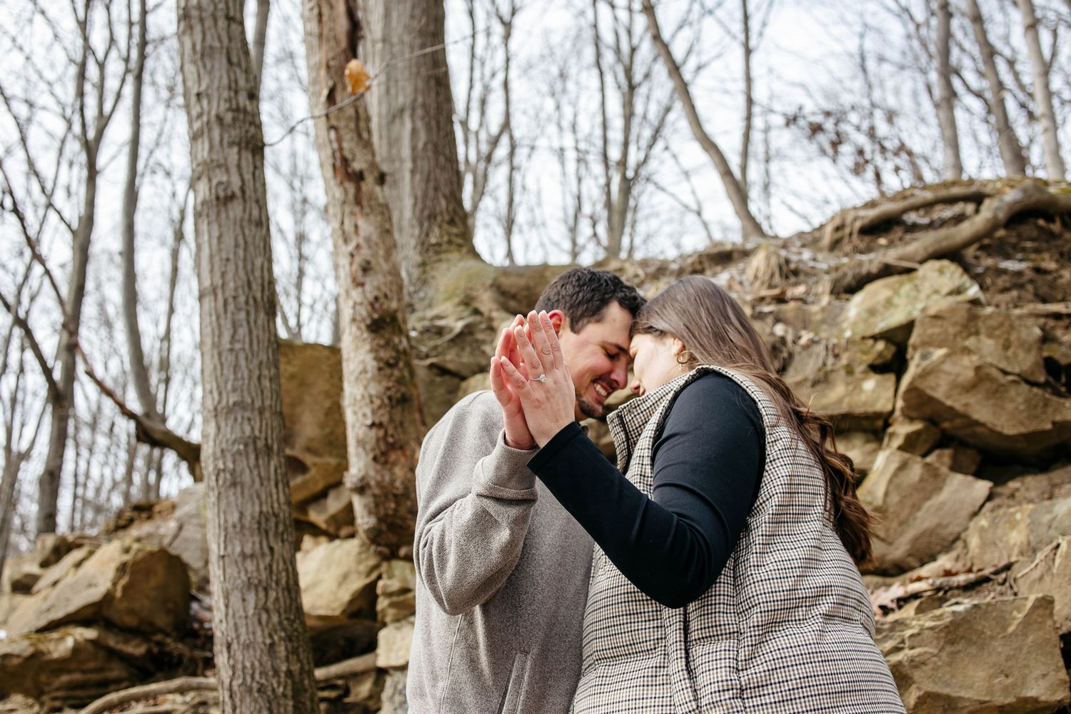 A couple shares an intimate moment in front of a rocky outcrop in a winter forest setting.