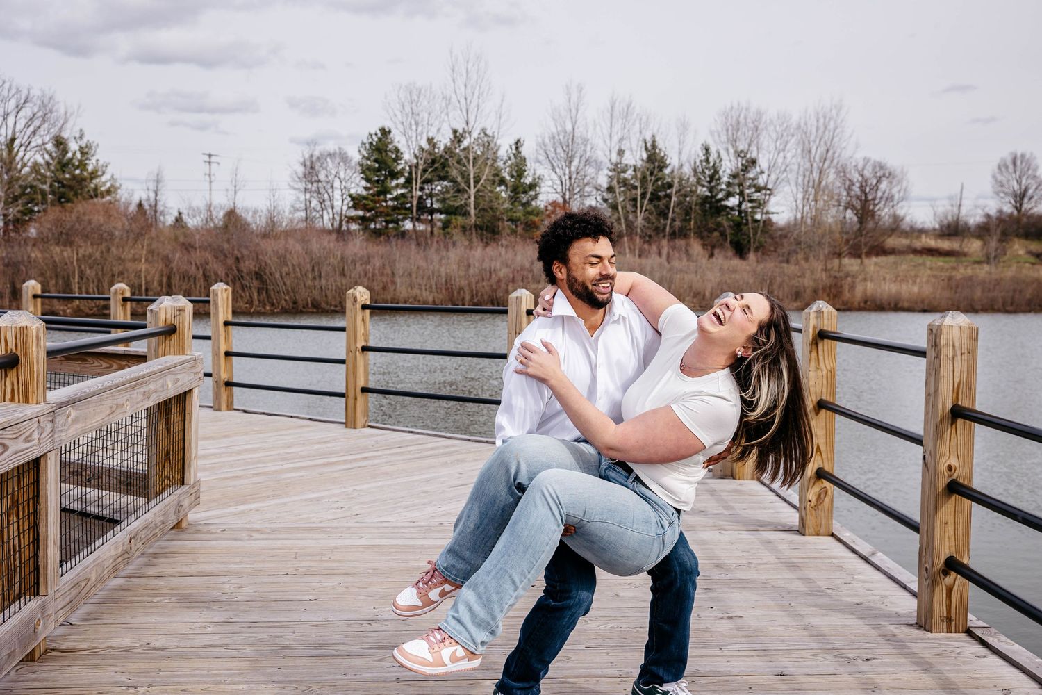 A couple shares a romantic moment while dancing and dipping on a wooden boardwalk surrounded by nature.