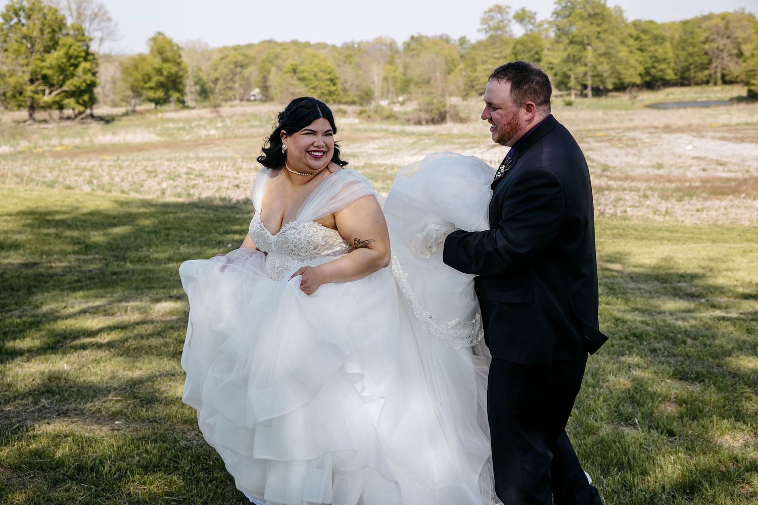 Two people in formal wedding attire share a joyful moment together in a sunny outdoor field.