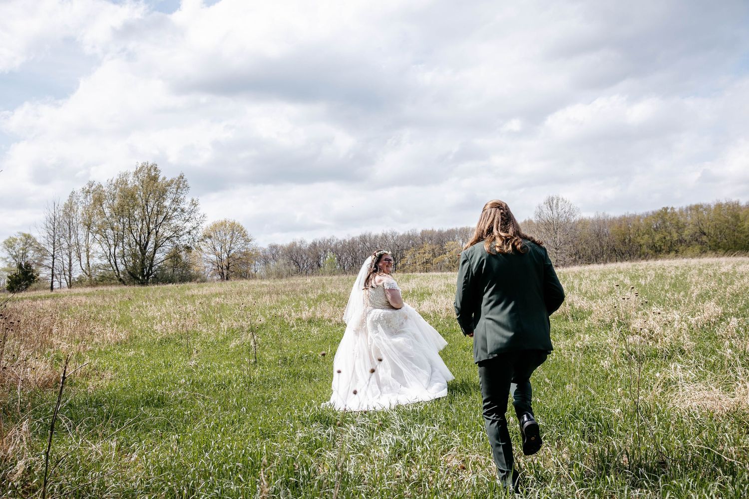 Two people run through a grassy meadow on a cloudy day, with trees visible in the background.