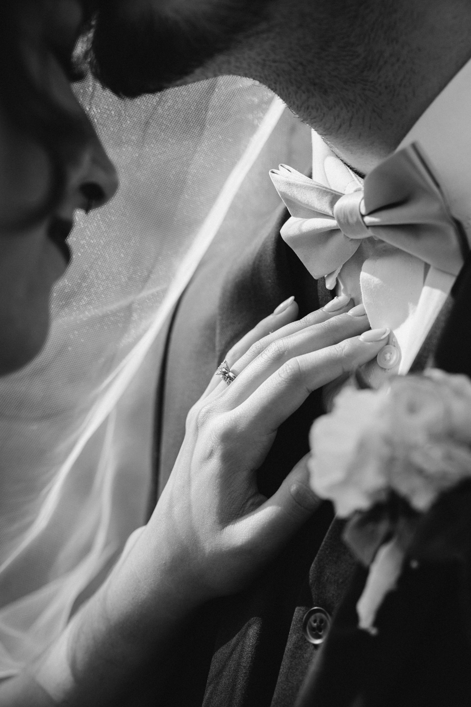 Close-up black and white photo of hands adjusting a formal bowtie with delicate details.