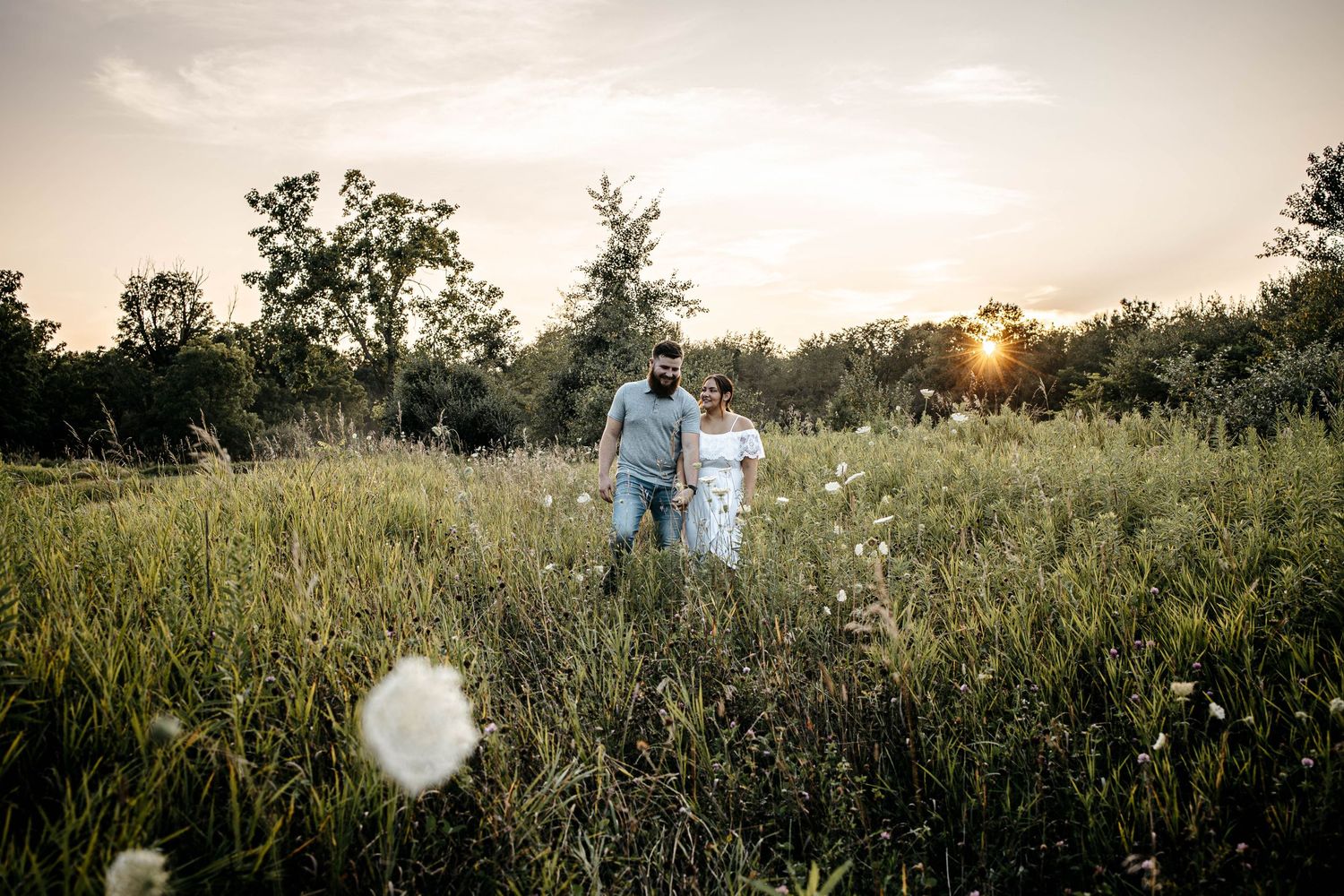 A couple strolls through a serene wildflower meadow at sunset as golden light filters through the trees.