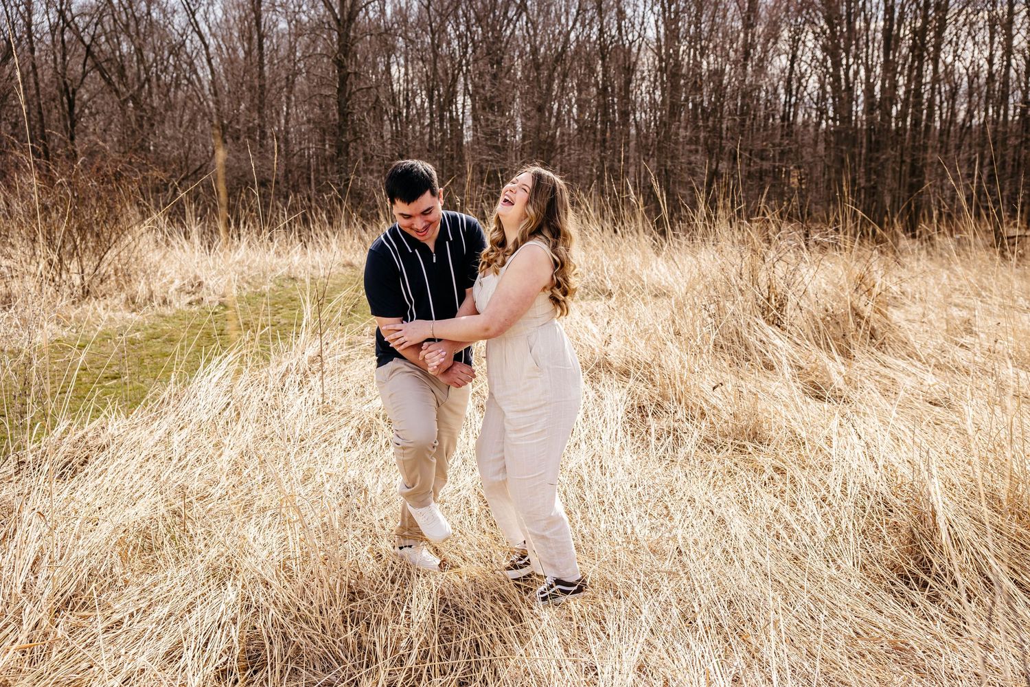 A couple holding hands and walking through tall golden grass in a natural field during autumn.