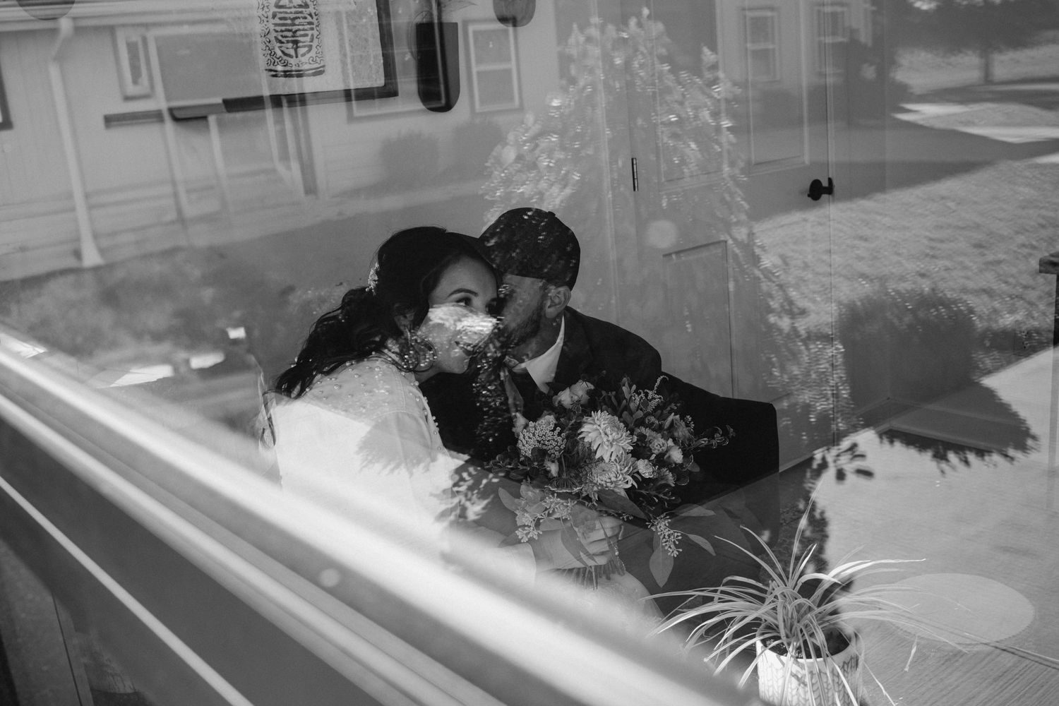 A romantic black and white reflection shows a tender moment through a window with flowers visible in the foreground.