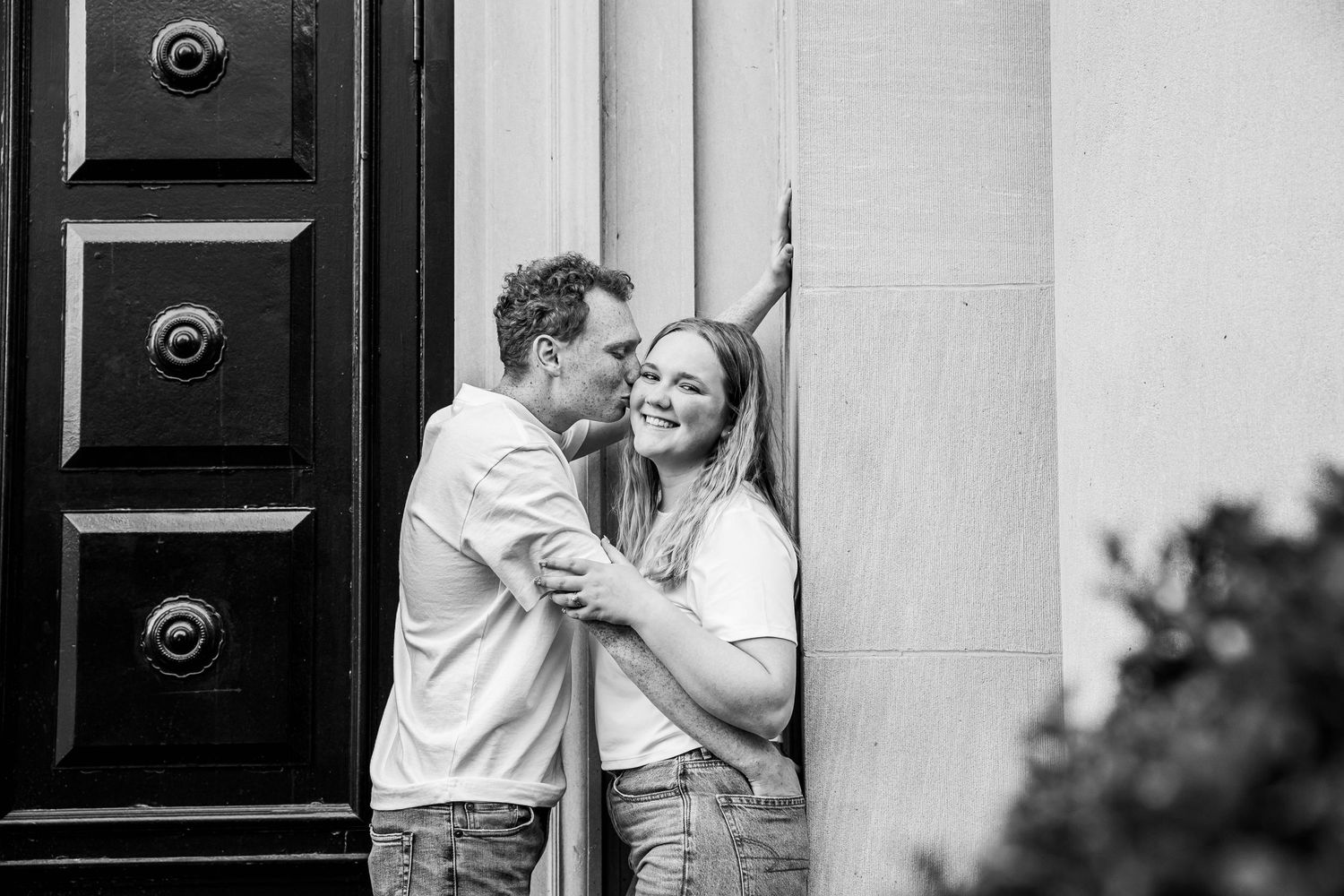A joyful black and white photo of a couple laughing together in a doorway.