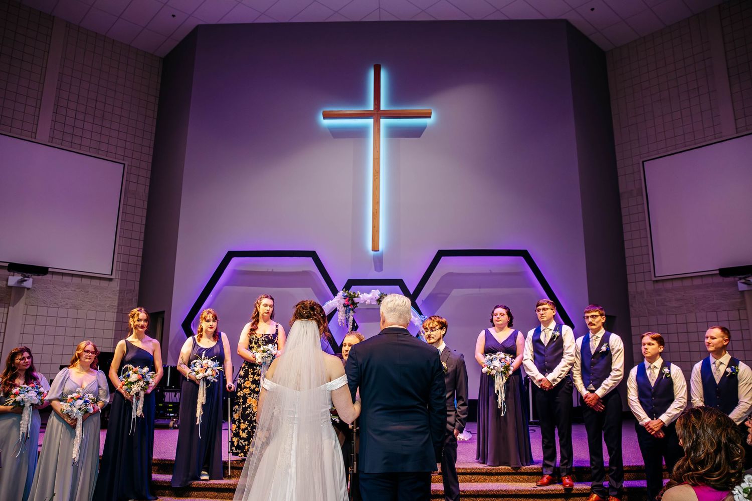 A group of people standing in a church sanctuary with illuminated crosses and purple lighting during a ceremony.