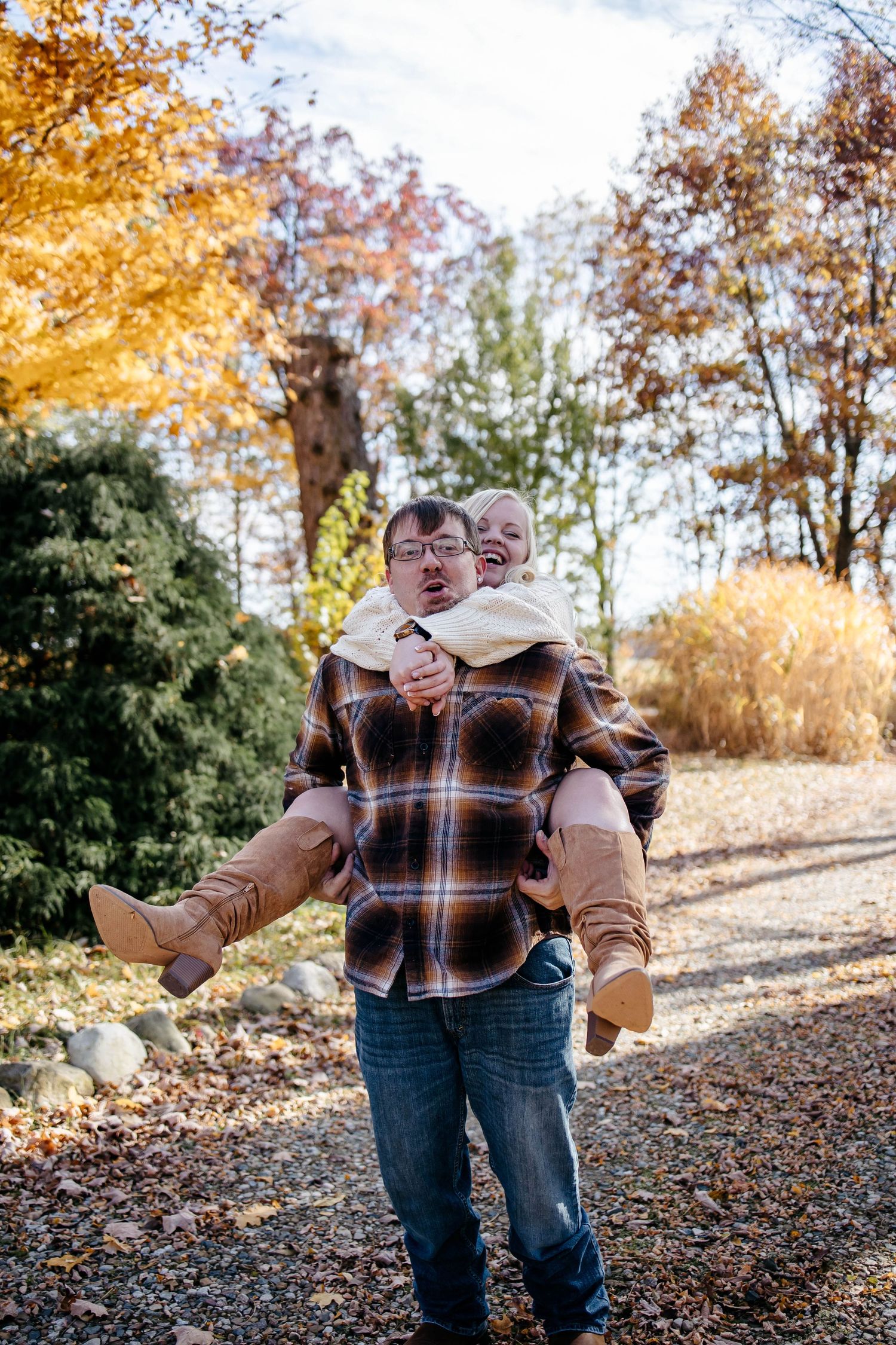 Two people share a playful moment on an autumn path surrounded by golden fall foliage and fallen leaves.