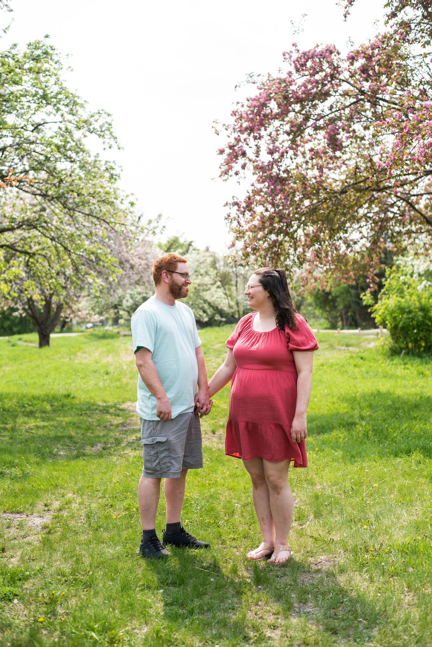 Two people standing in a blooming spring orchard with pink blossoms and lush green grass.