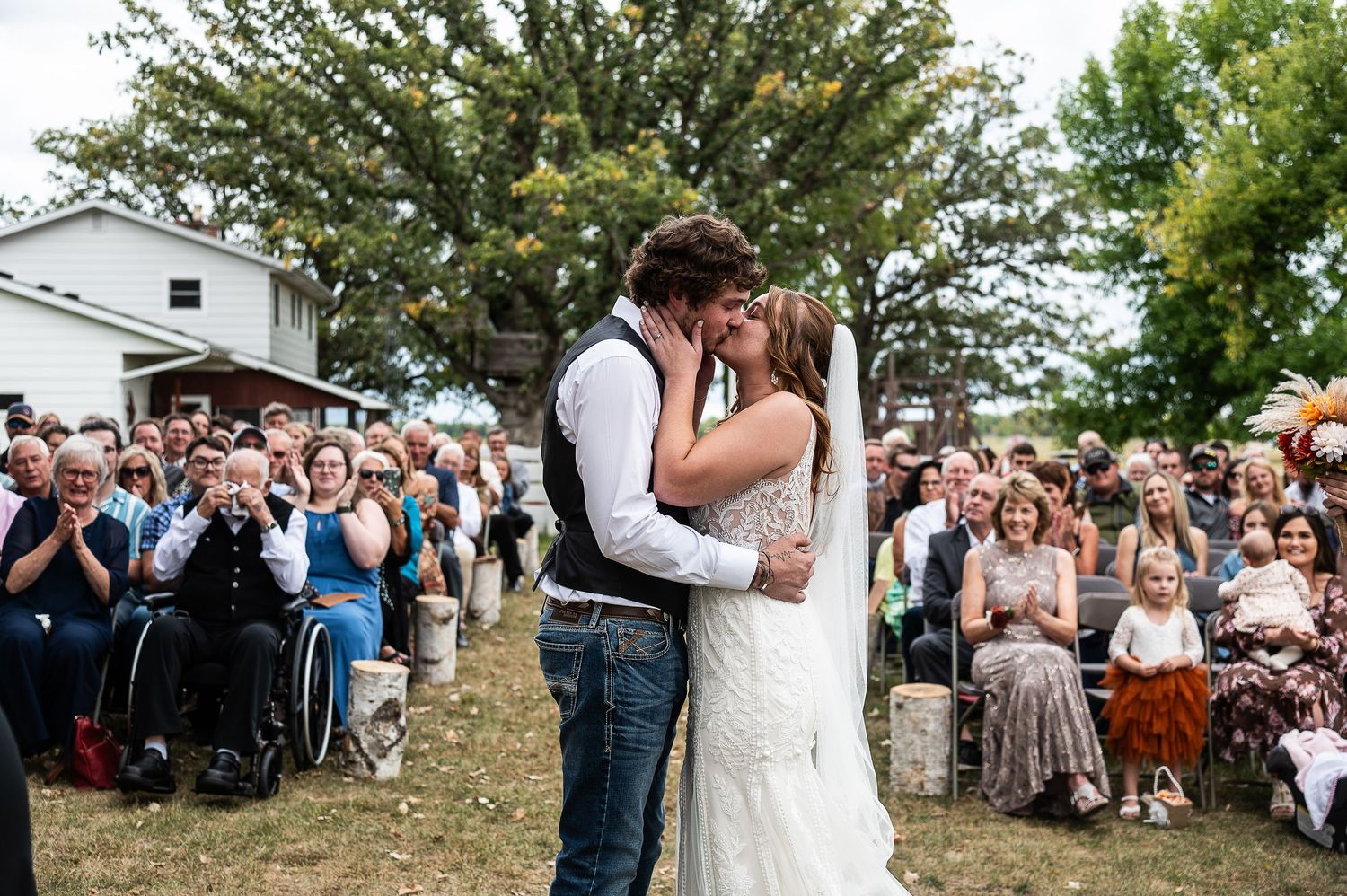 Outdoor wedding ceremony with guests seated in rows beneath large trees.