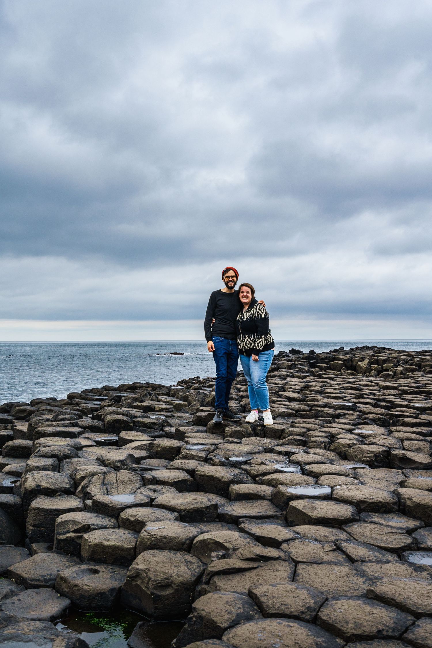 Tourists stand on the unique hexagonal basalt columns at Giant's Causeway in Northern Ireland under moody skies.