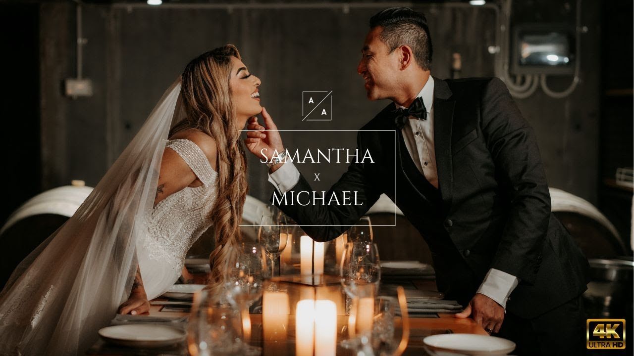 A bride and groom share a candlelit moment at a reception table with her veil flowing behind them.