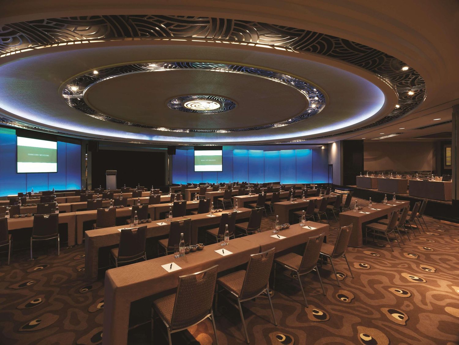 A modern conference room with circular ceiling design features long tables, overhead lighting and blue-lit wall displays.