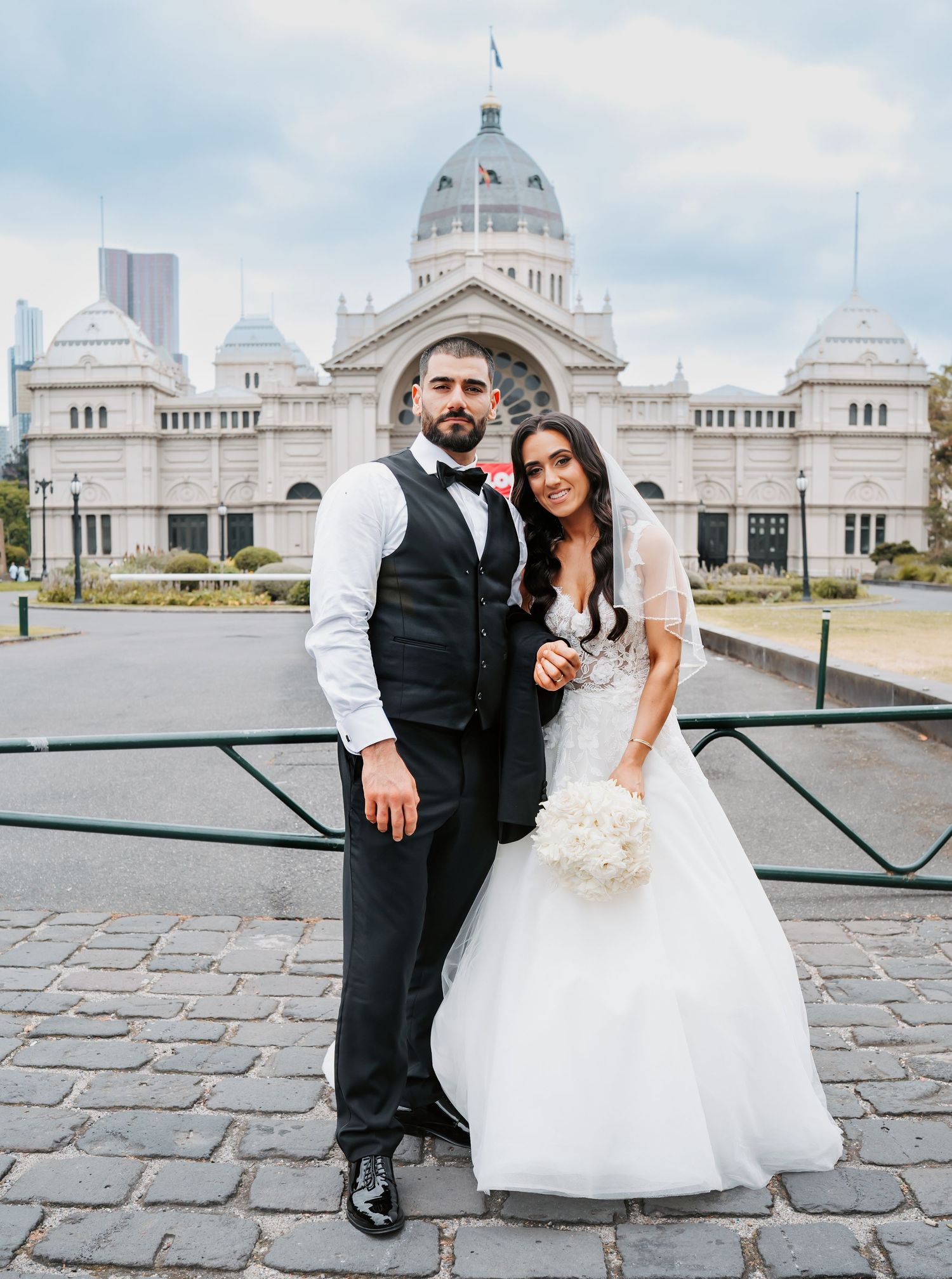 A bride and groom pose together outside the beautiful Royal Exhibition Building in Melbourne with its ornate domed architecture.