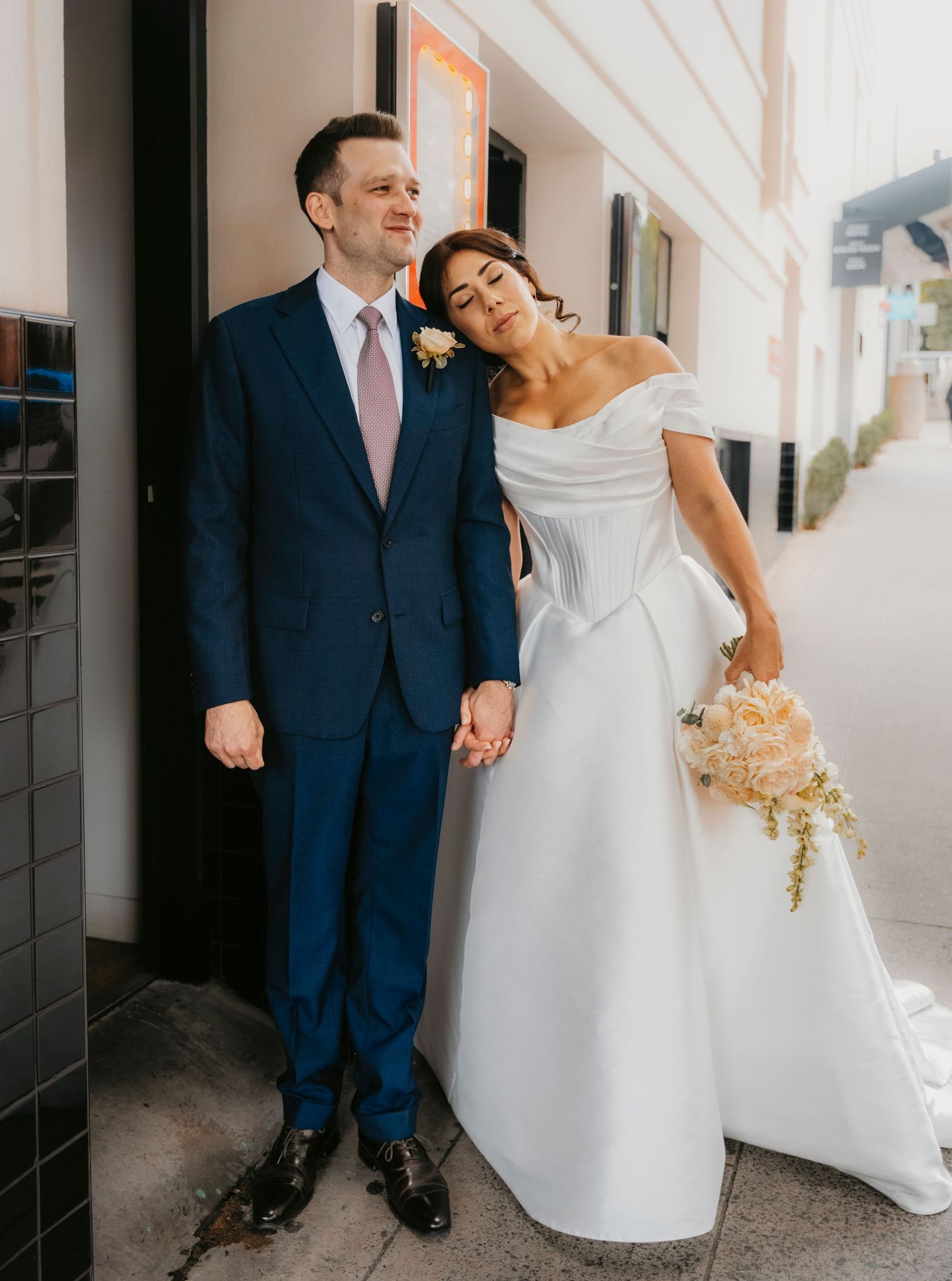A couple in wedding attire poses together on their special day, with the bride in white and groom in navy blue suit.