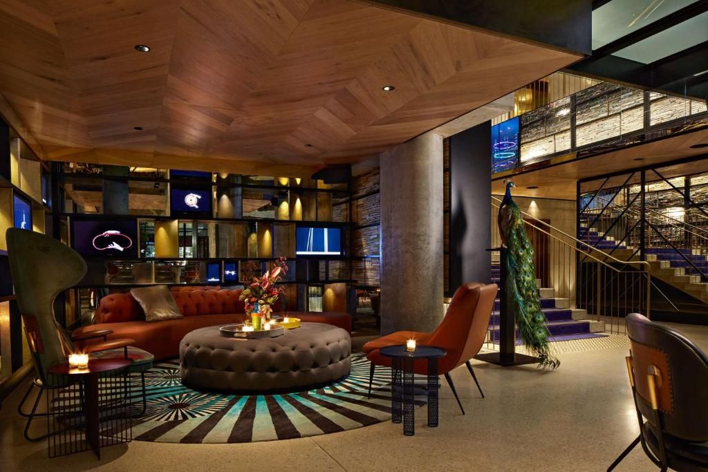 Modern hotel lobby lounge with wood ceiling, leather seating, and geometric floor pattern illuminated by warm lighting.