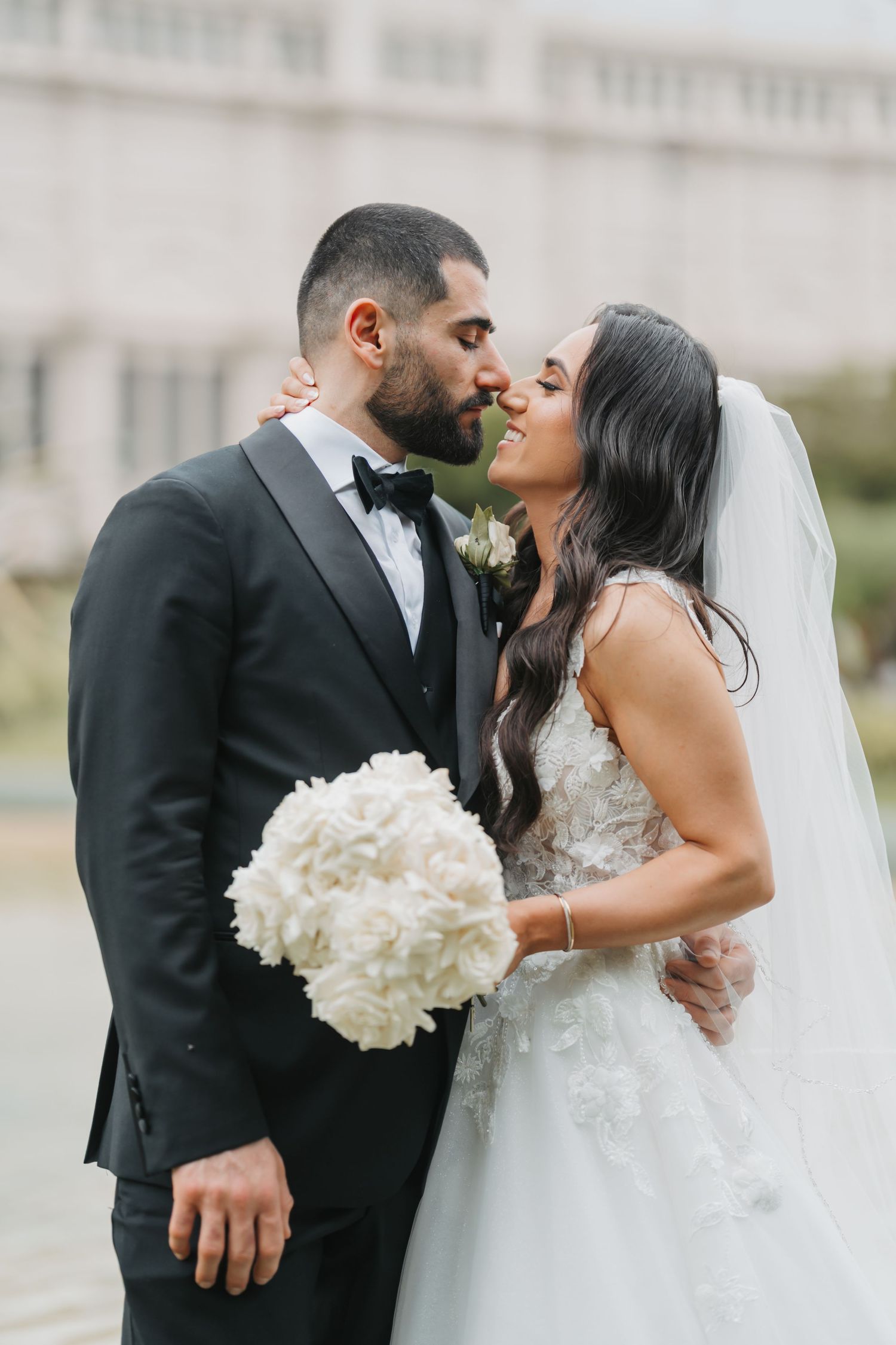 Newlywed couple shares intimate moment with bride holding white hydrangea bouquet in outdoor wedding setting.
