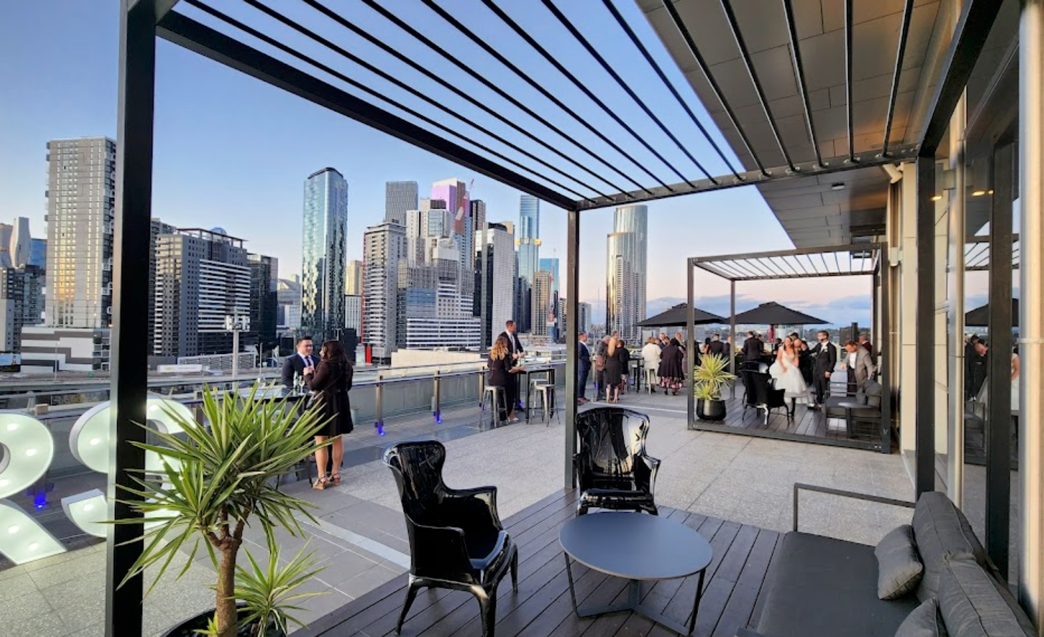 Modern rooftop terrace with city skyline view features covered seating area and potted plants in urban setting.