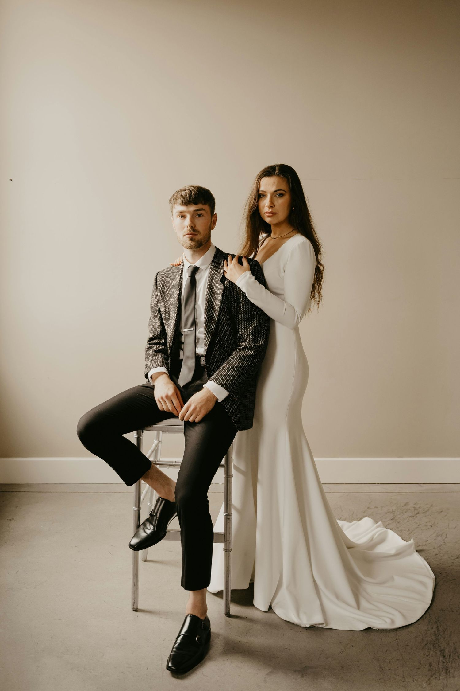 Modern minimalist wedding photography capturing couple in elegant white dress and gray suit against neutral studio background.