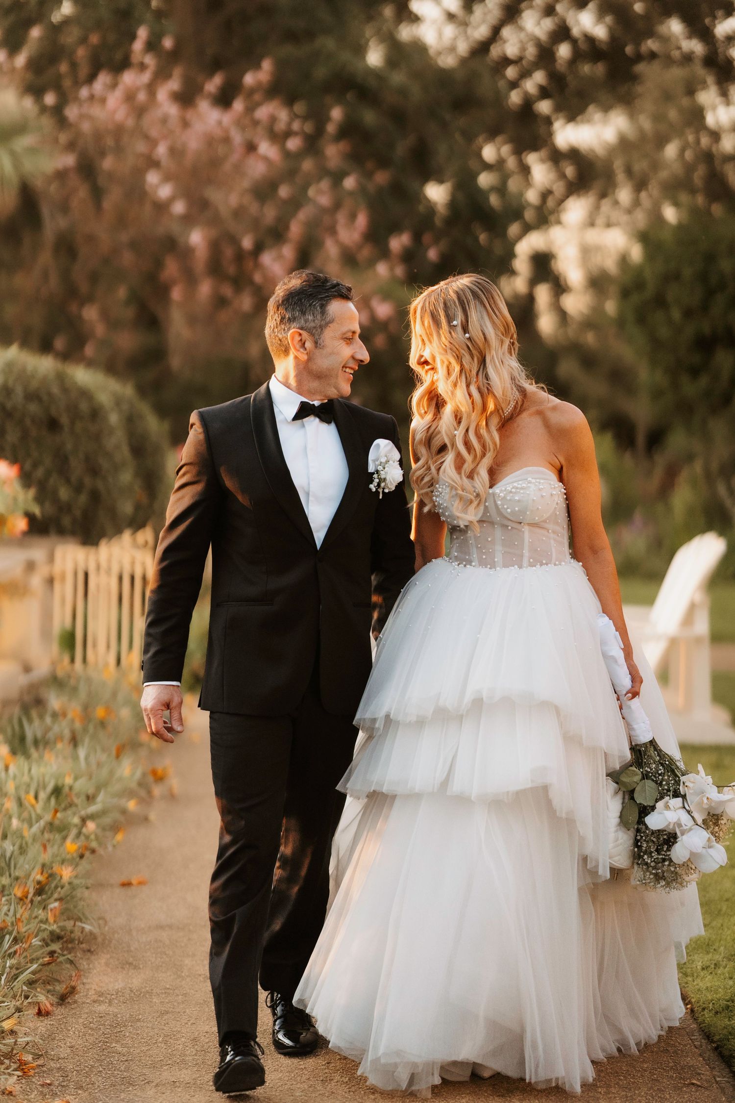 A couple sharing a romantic moment on their wedding day walking along a garden path at golden hour.