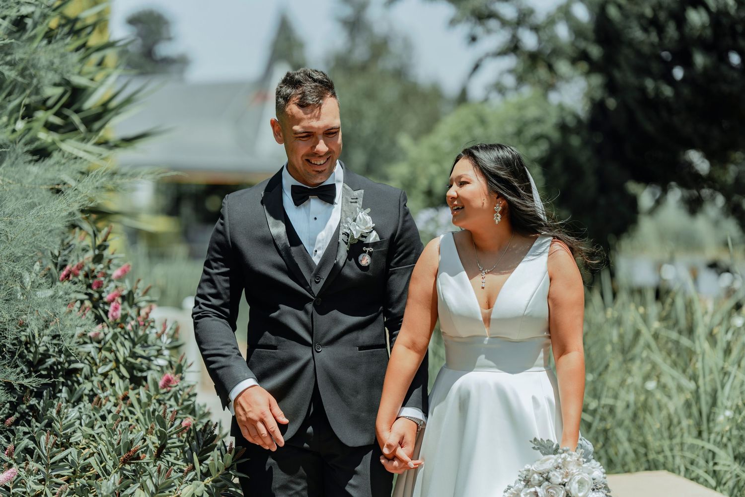 A couple shares a joyful moment together in a garden setting on their wedding day, surrounded by lush greenery.