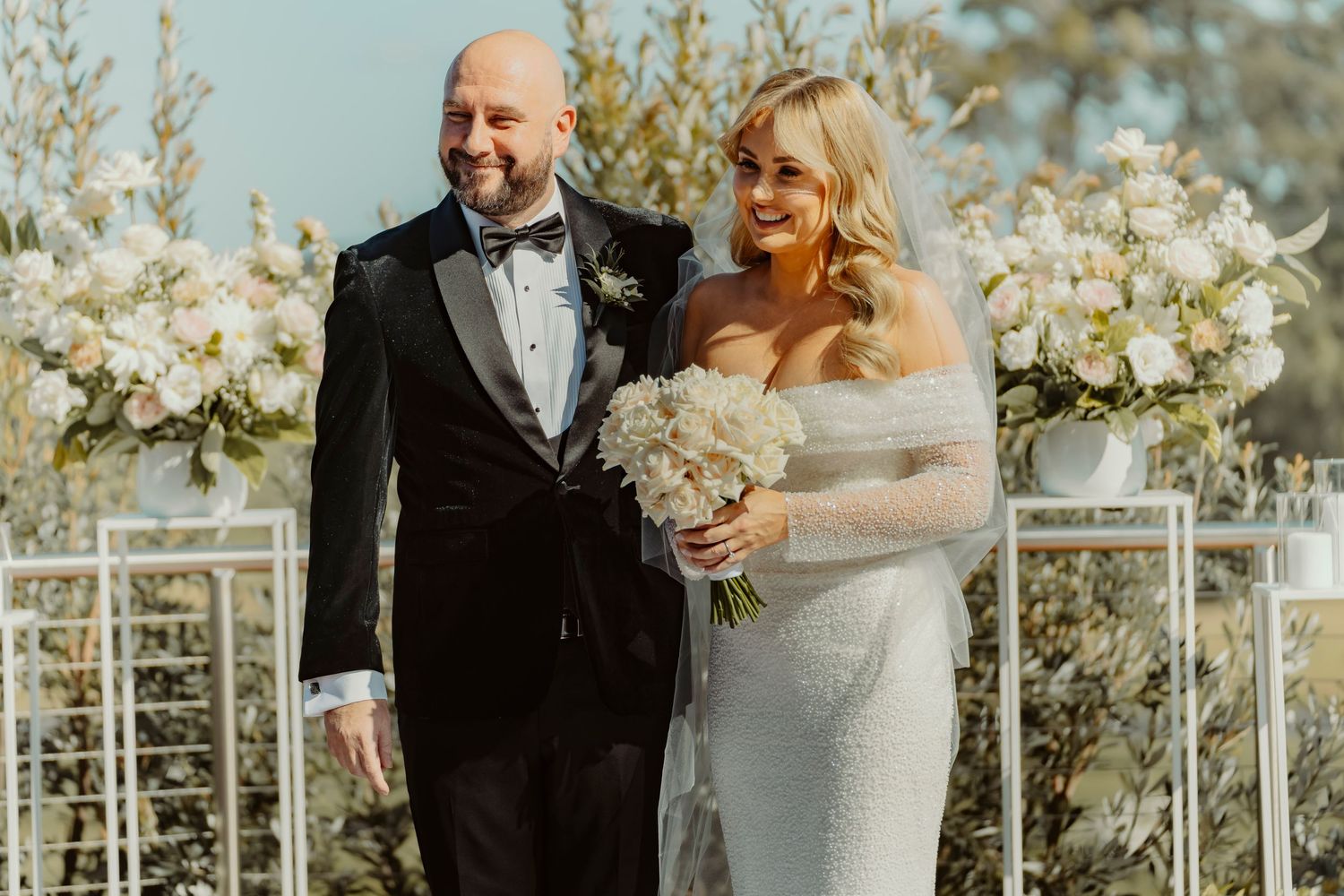 A joyful couple shares a candid moment together at their outdoor garden wedding ceremony surrounded by white floral arrangements.