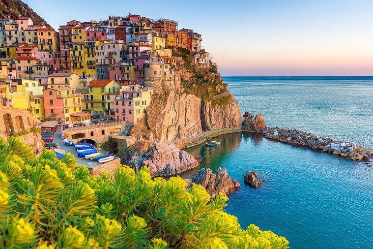 Colorful houses perched on cliffs overlooking turquoise Mediterranean waters in Cinque Terre, Italy at sunset.
