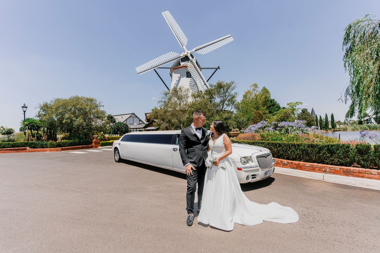 A couple poses by a white stretch limousine with a traditional Dutch windmill in the background.