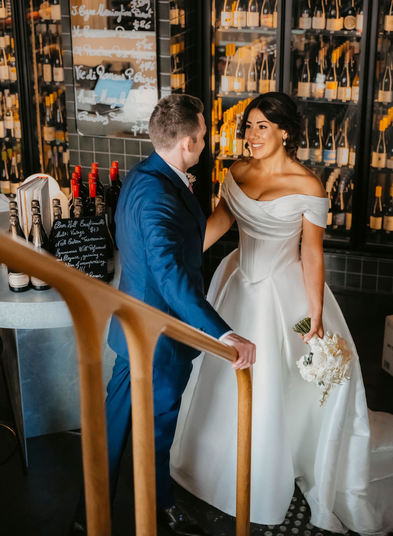 Elegant couple share a special moment at a wine bar backdrop with decorative wine bottles and ambient lighting.