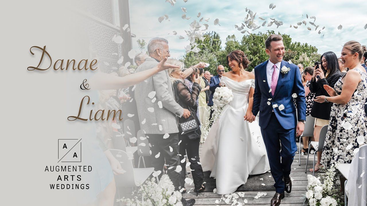 Wedding guests toss confetti over a newlywed couple exiting their ceremony along a garden path on a sunny day.