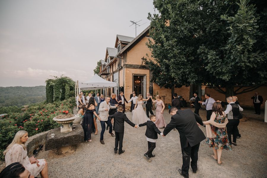 Wedding guests dance on the terrace of a hilltop venue with scenic mountain views in the background.