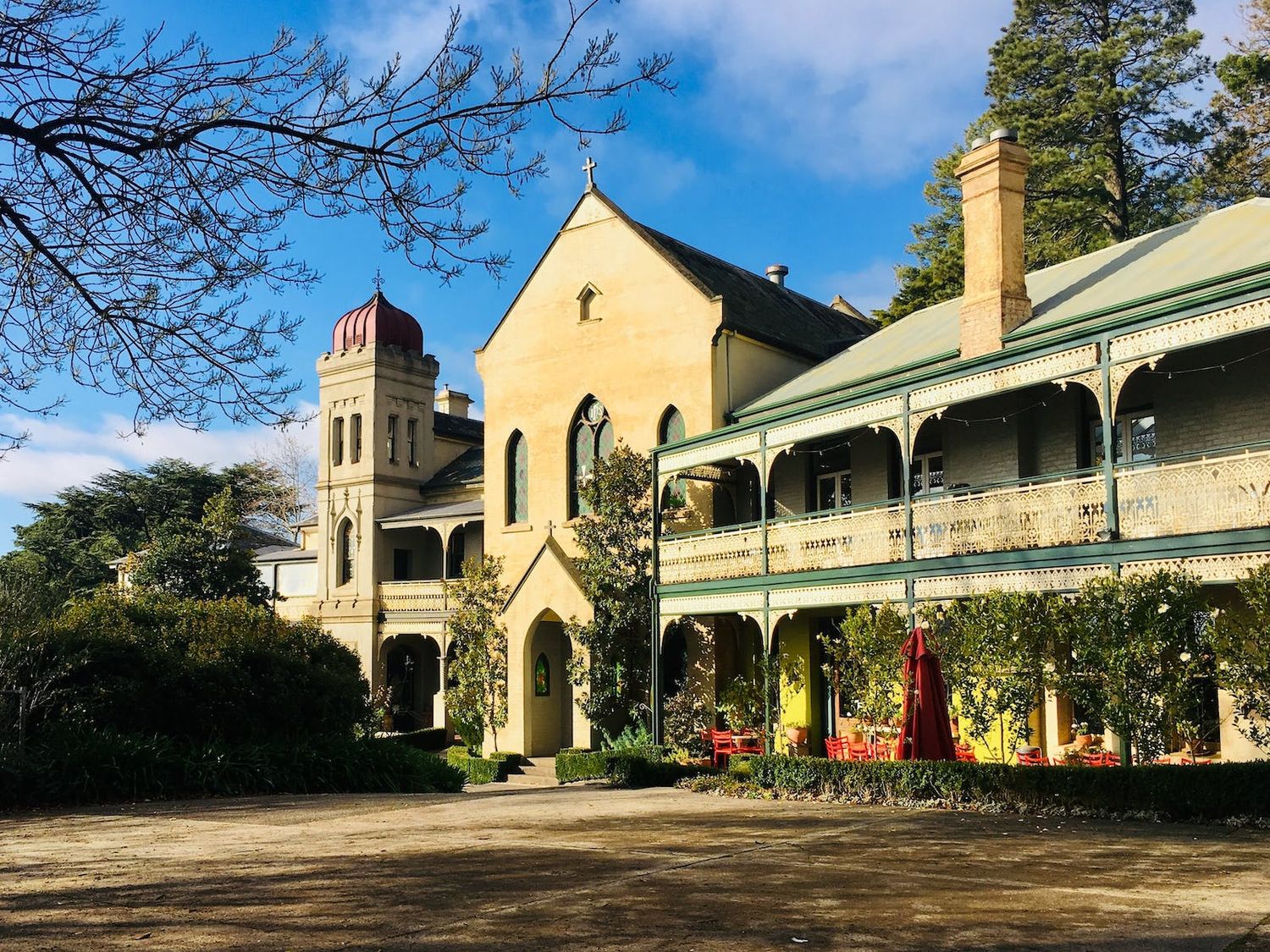 Historic stone church building with Gothic architecture and covered veranda in warm sunlight against blue sky background.