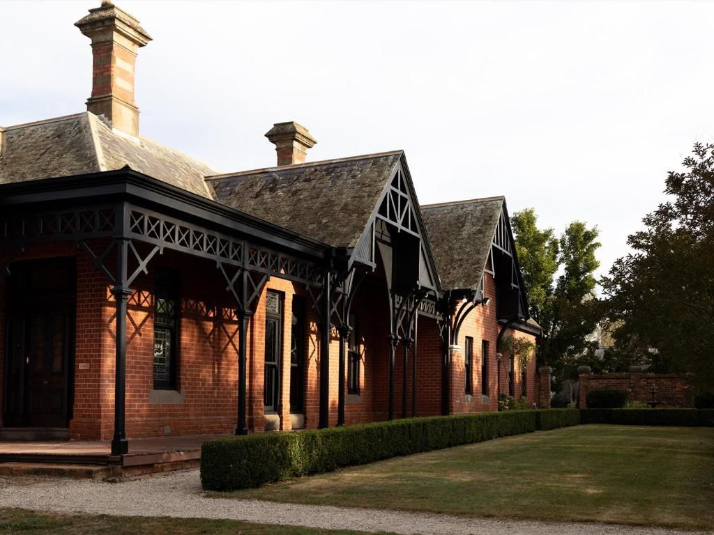 Historic Victorian brick cottage with ornate wooden trim and peaked roofs sits on manicured lawn at dusk.