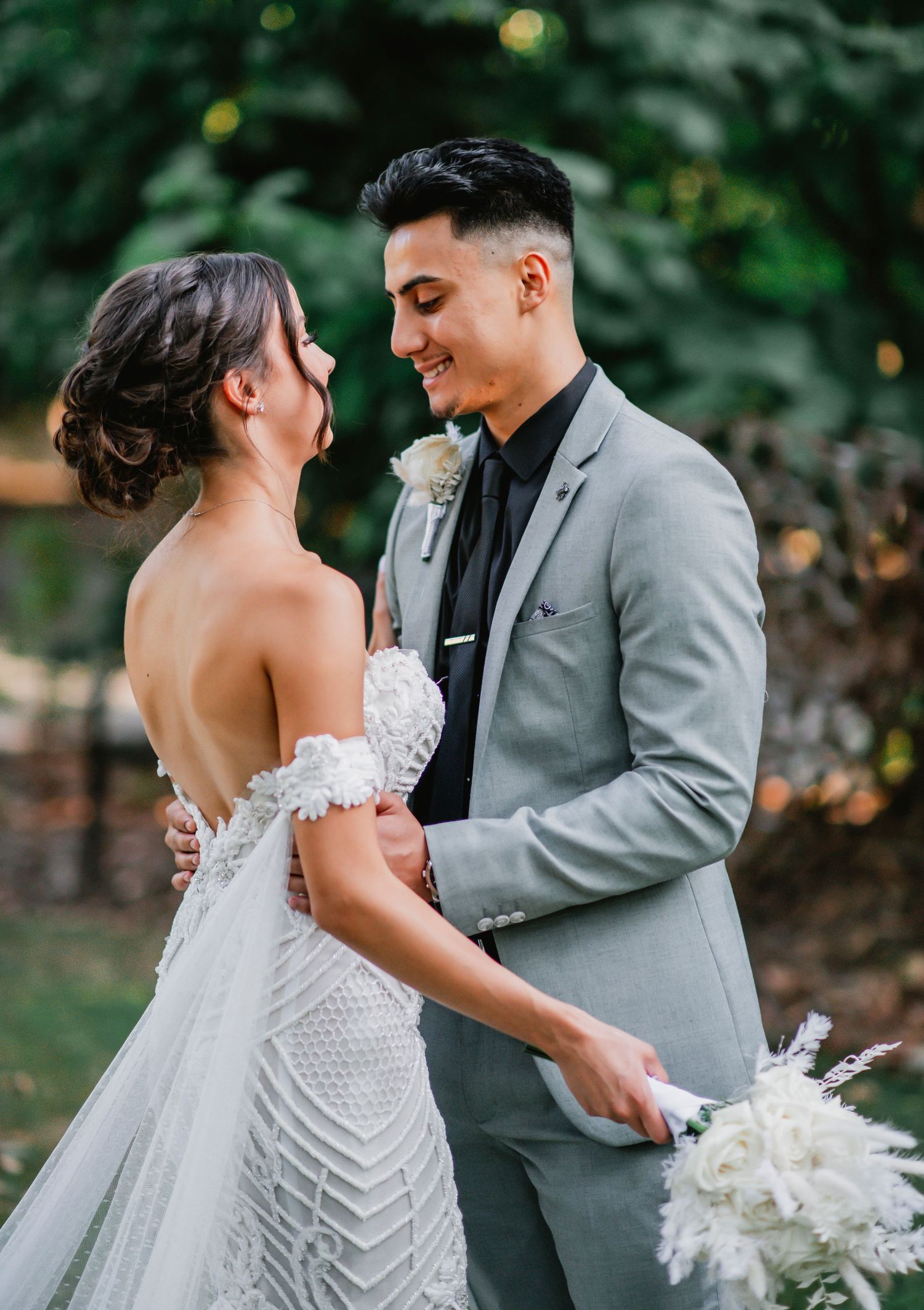 A romantic moment between newlyweds at an outdoor garden wedding, with the bride in a geometric lace gown and groom in grey suit.