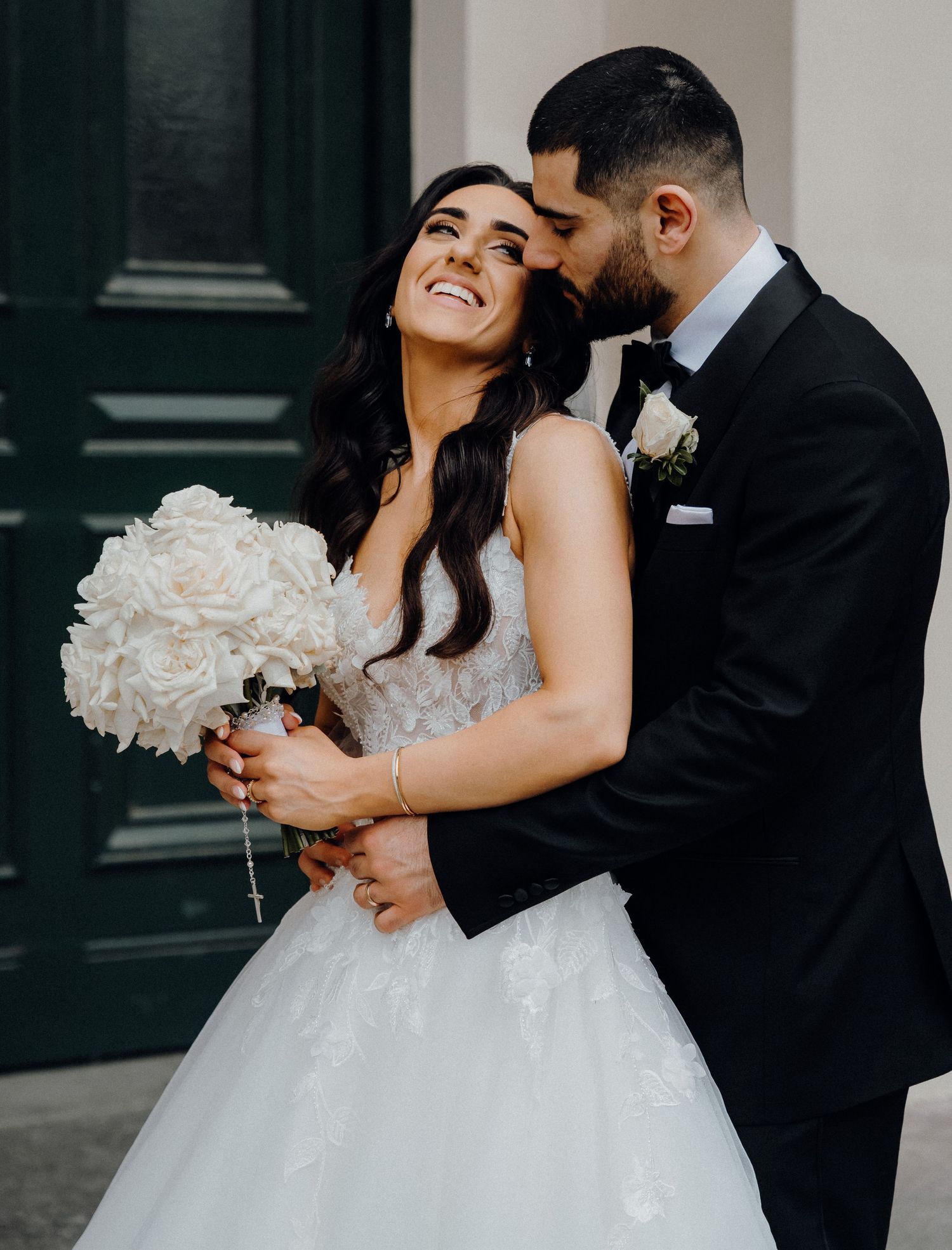 A joyful couple shares an intimate moment on their wedding day with white bouquet and formal attire.