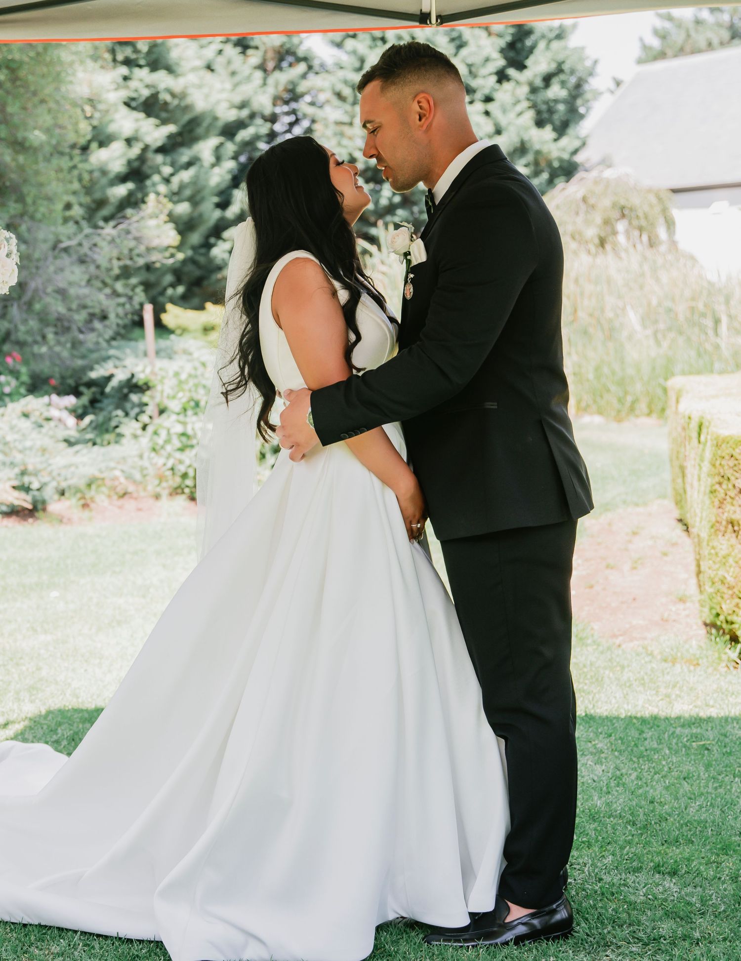 A bride and groom share an intimate moment during their wedding ceremony on a lush green lawn.