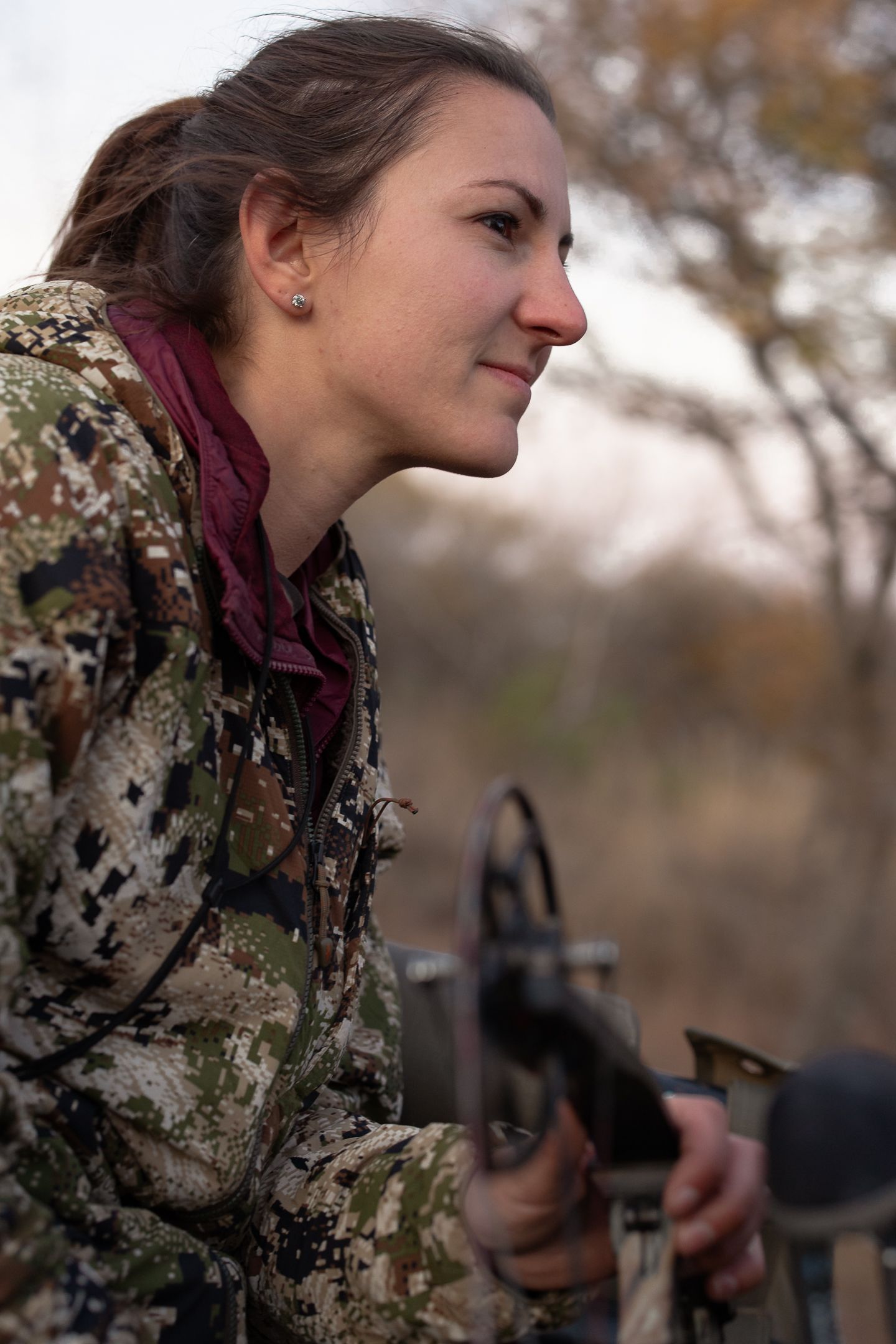 side profile of woman wearing camo holding bow and looking off into distance