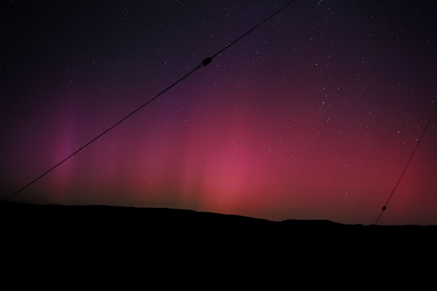 Beautiful pink and purple aurora borealis displays across dark night sky with silhouetted mountain landscape below.