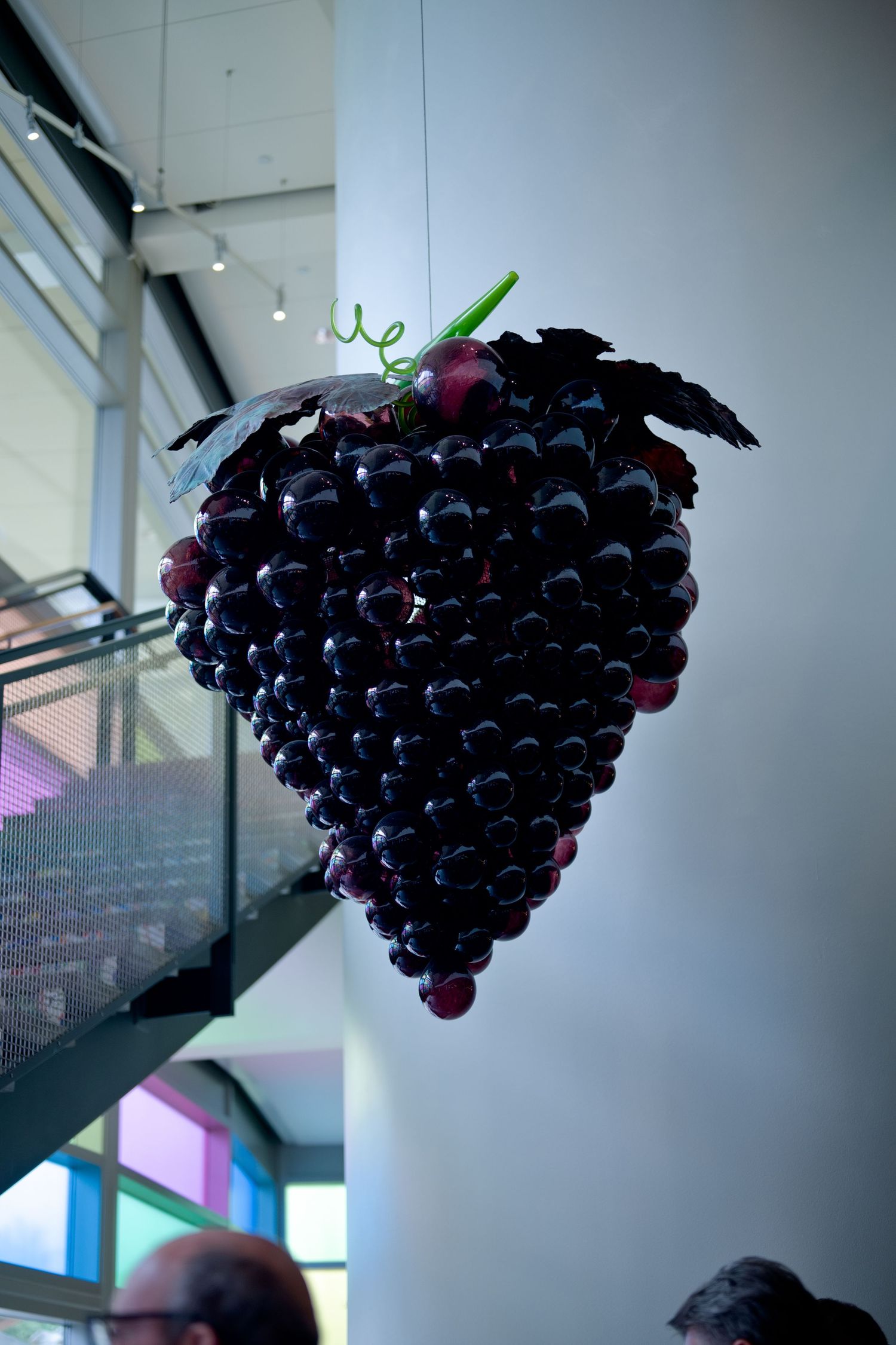 A large decorative bunch of dark purple grapes hangs from the ceiling in an art installation space.