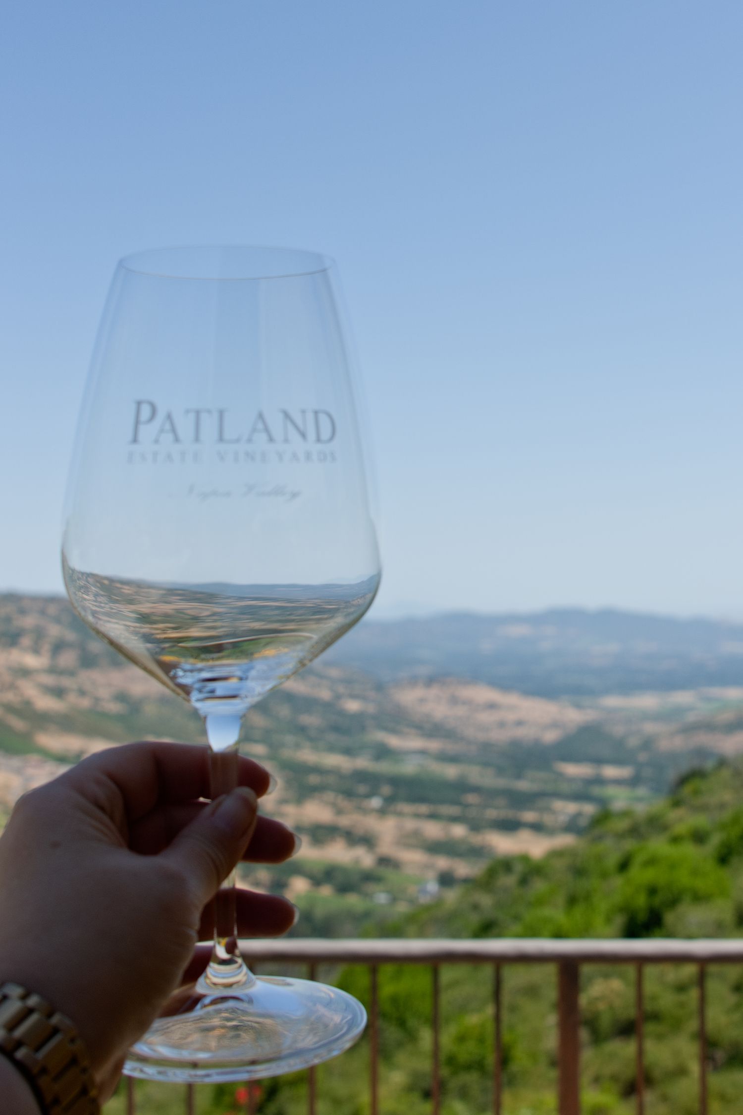 A wine glass held against a scenic mountain vista with rolling hills, captured from Patland Estate Winery in the Soda Canyon hills of Napa
