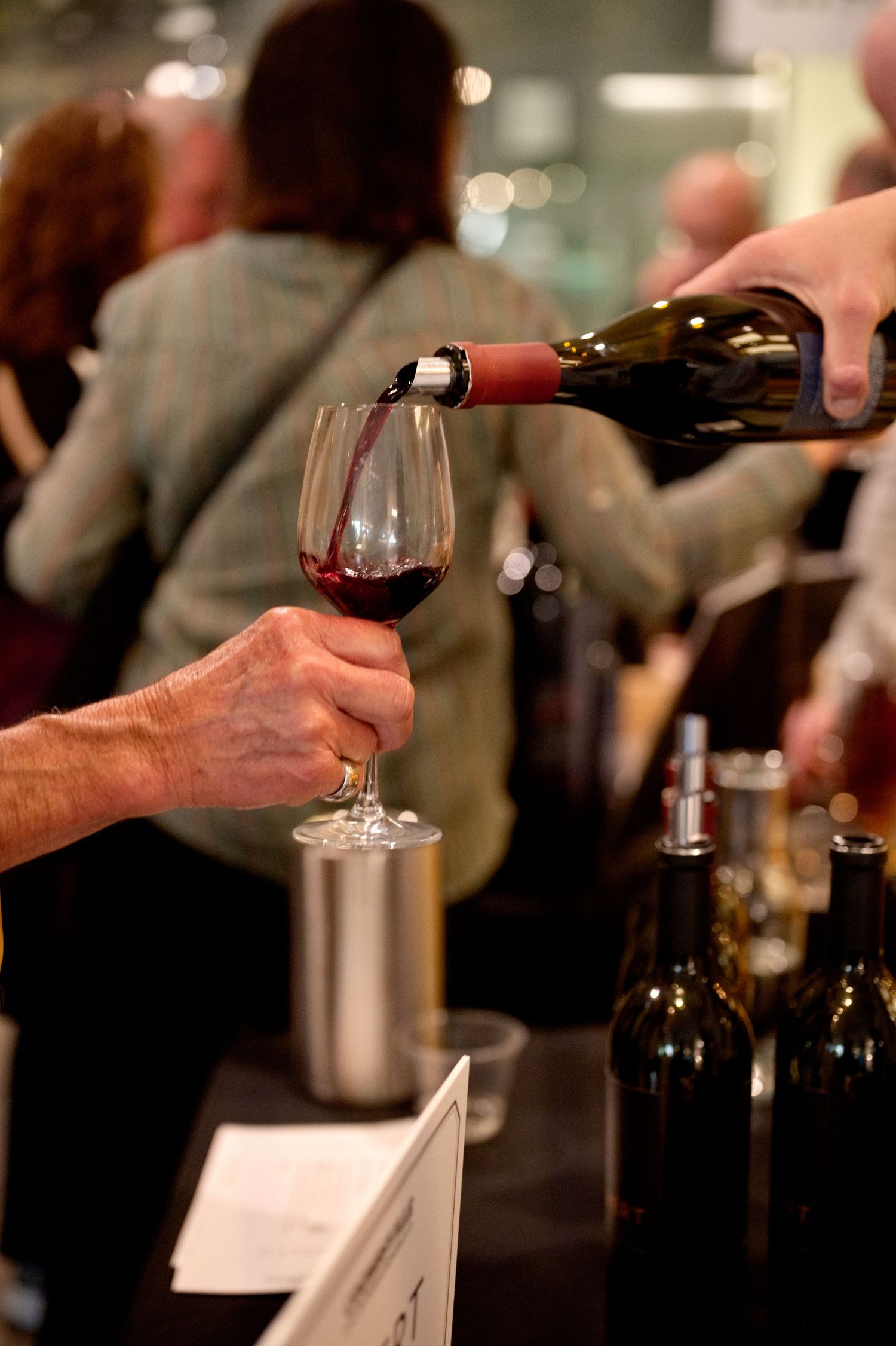 Red wine being poured into a wine glass during a wine tasting event at a dimly lit bar.