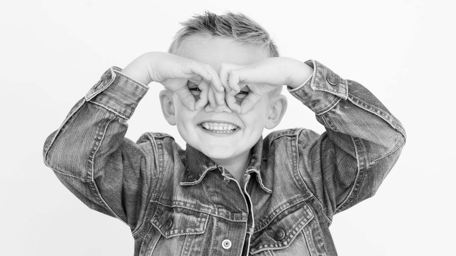 A playful black and white image showing a person making binocular shapes with their hands while wearing a denim jacket.