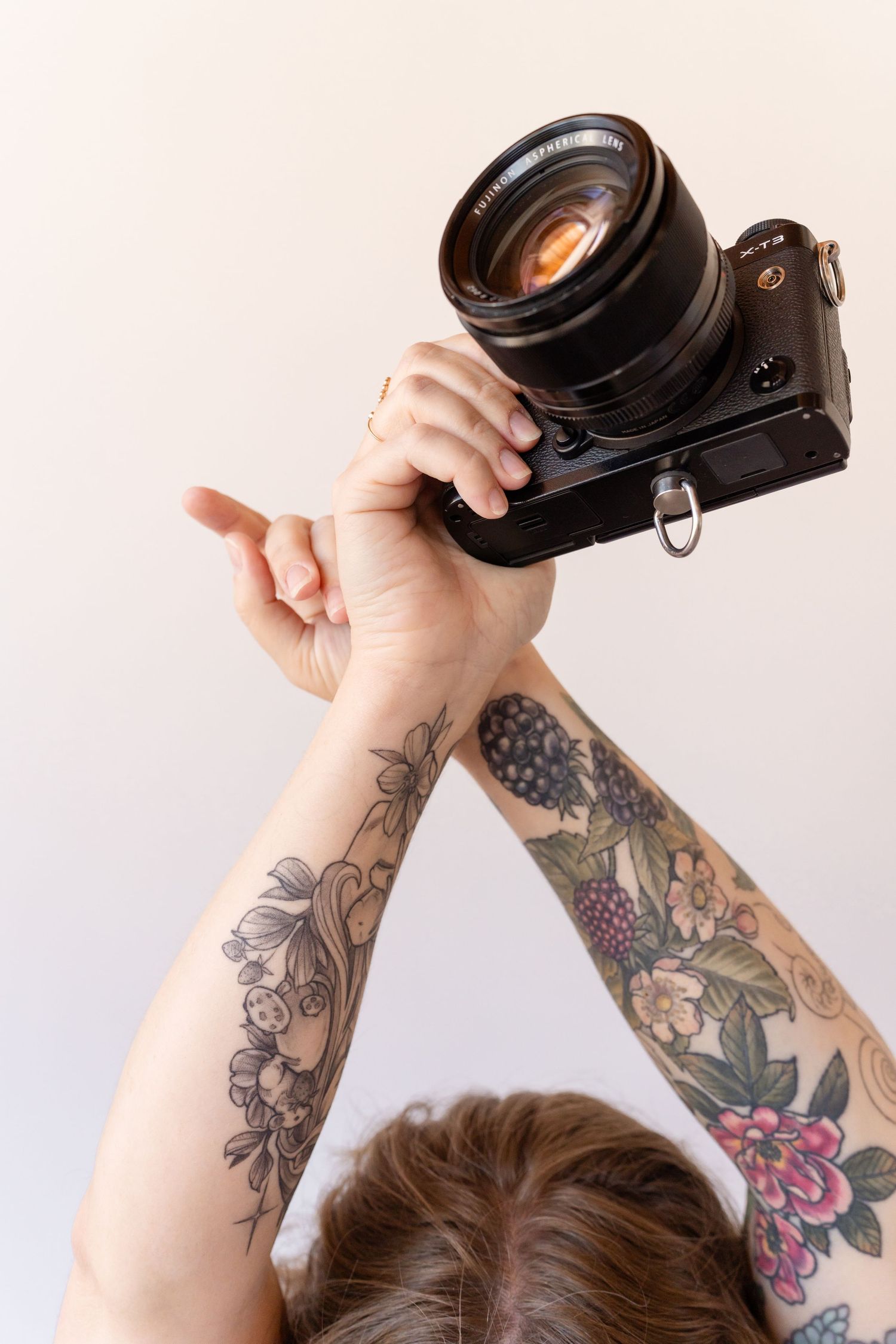 Photographer with colorful floral tattoos holding up a professional camera against white background.