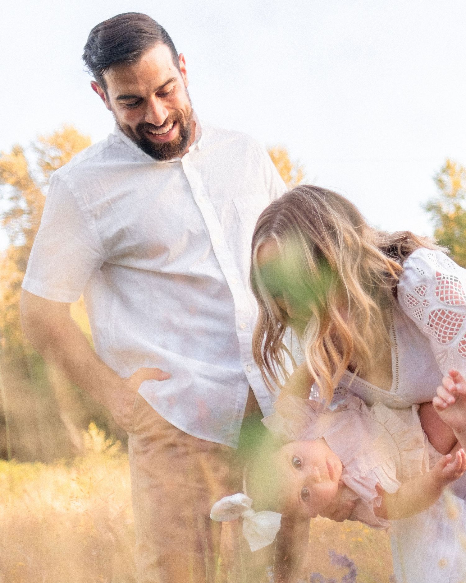 A happy family plays together in a sunlit field with golden grass and trees at sunset.