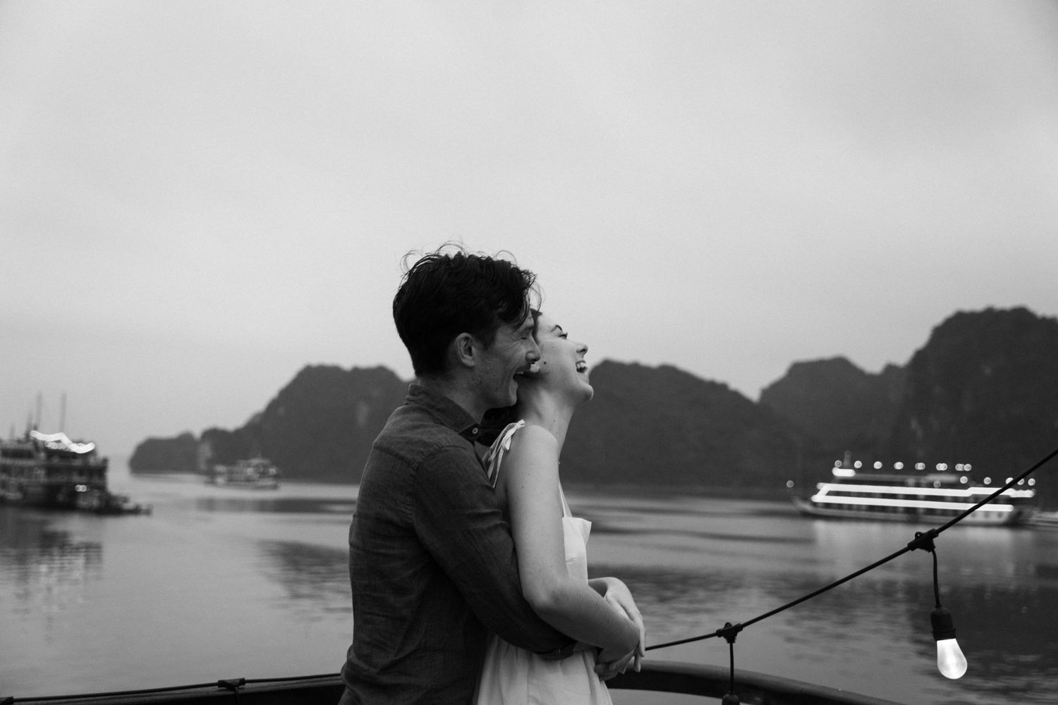 Romantic couple sharing an intimate moment by a misty harbor with mountains in the background.