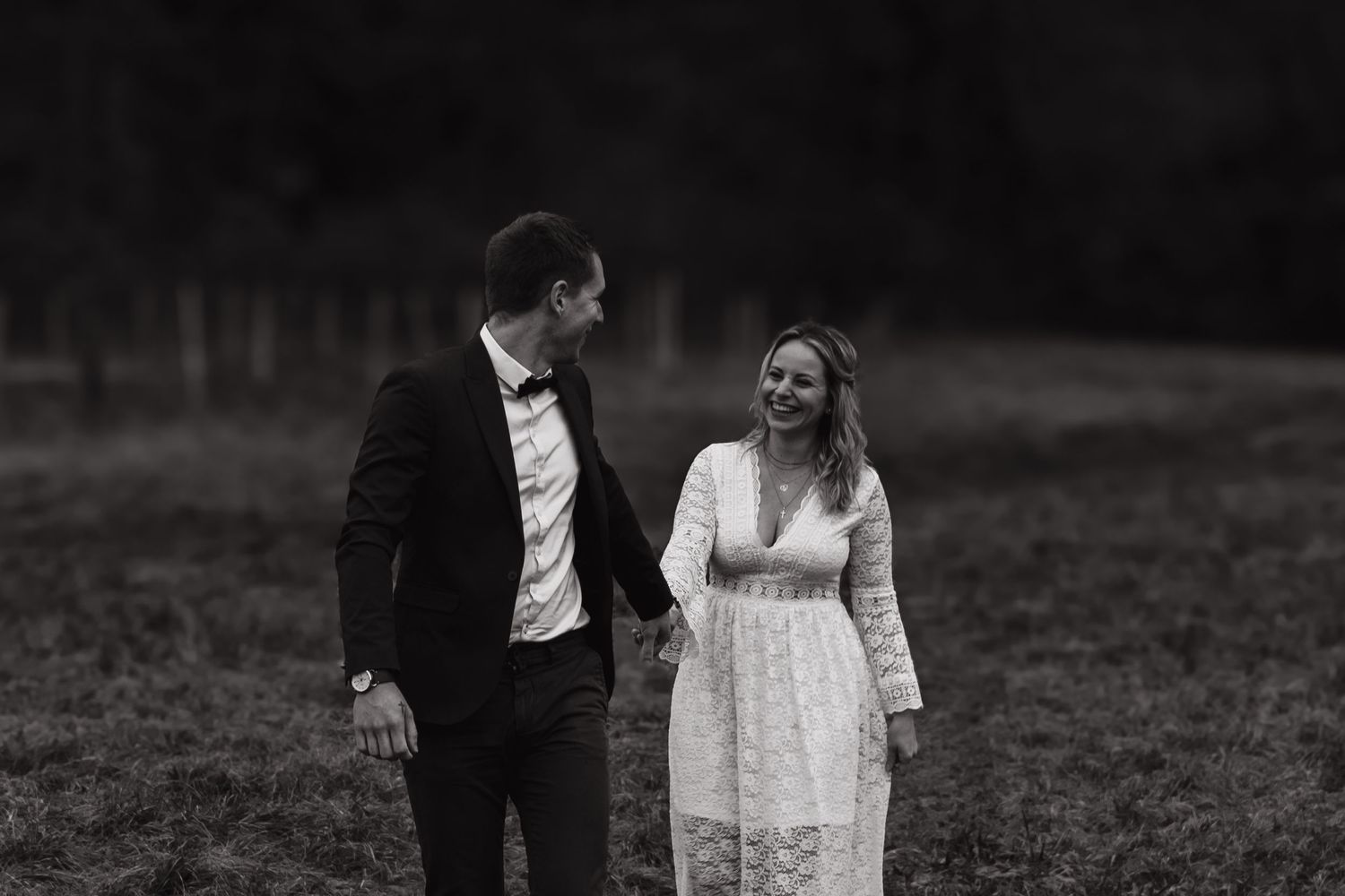 A black and white wedding portrait of a couple in formal attire standing together in a field.