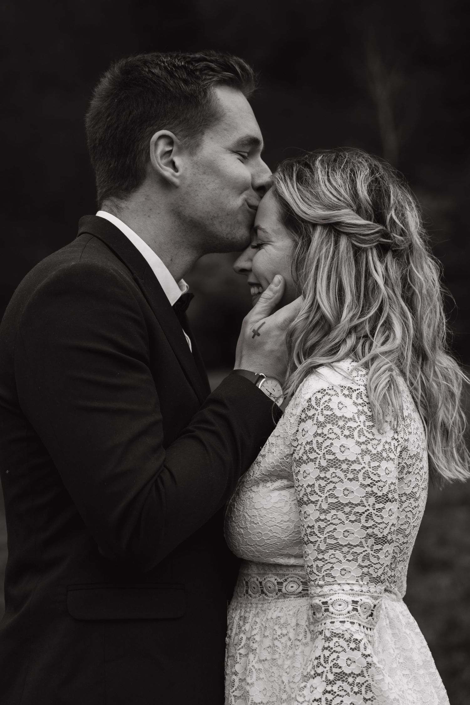 An intimate black and white portrait of a couple sharing a tender moment in formal wedding attire.