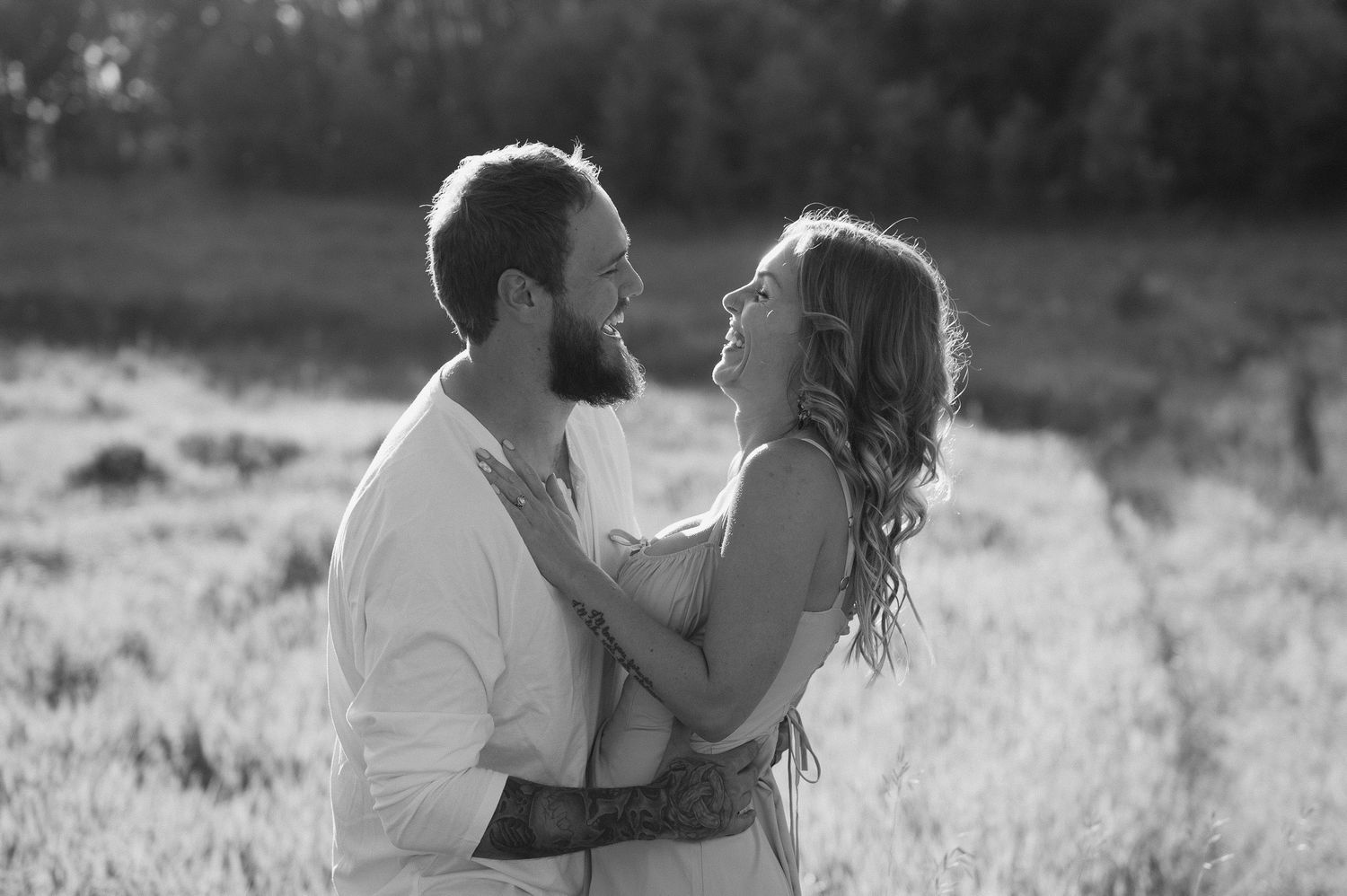 A romantic couple embraces and shares intimate moments in a grassy meadow during a black and white outdoor photoshoot.