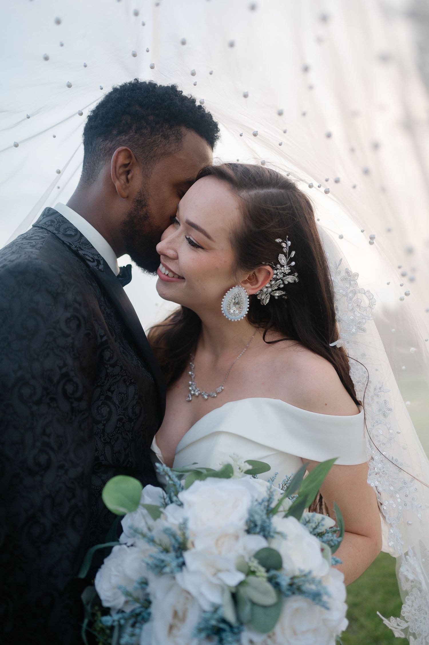 A bride and groom share a tender moment during their wedding day photoshoot with white floral bouquet.