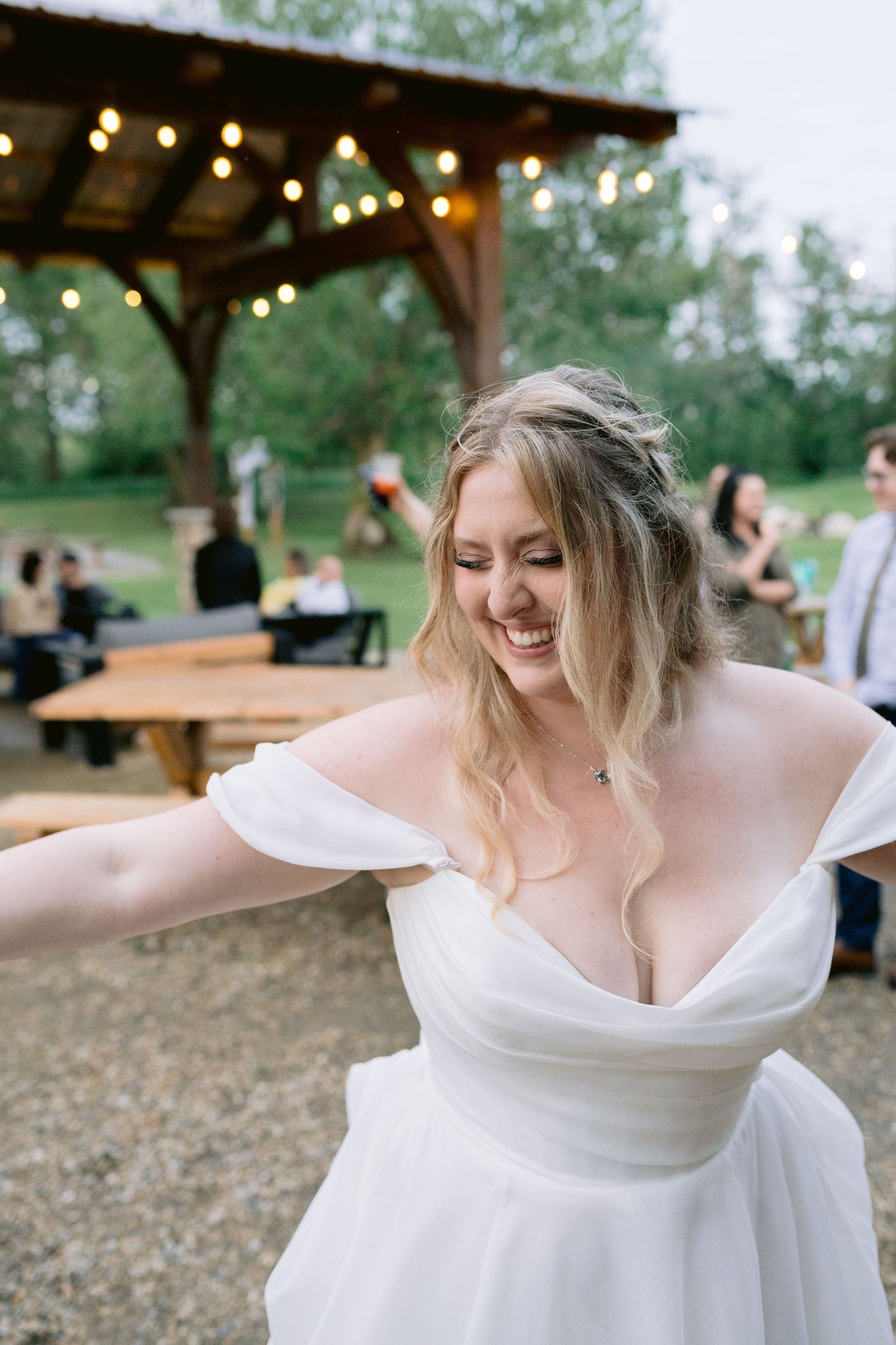 Bride in white dress twirls and dances under string lights at an outdoor reception.